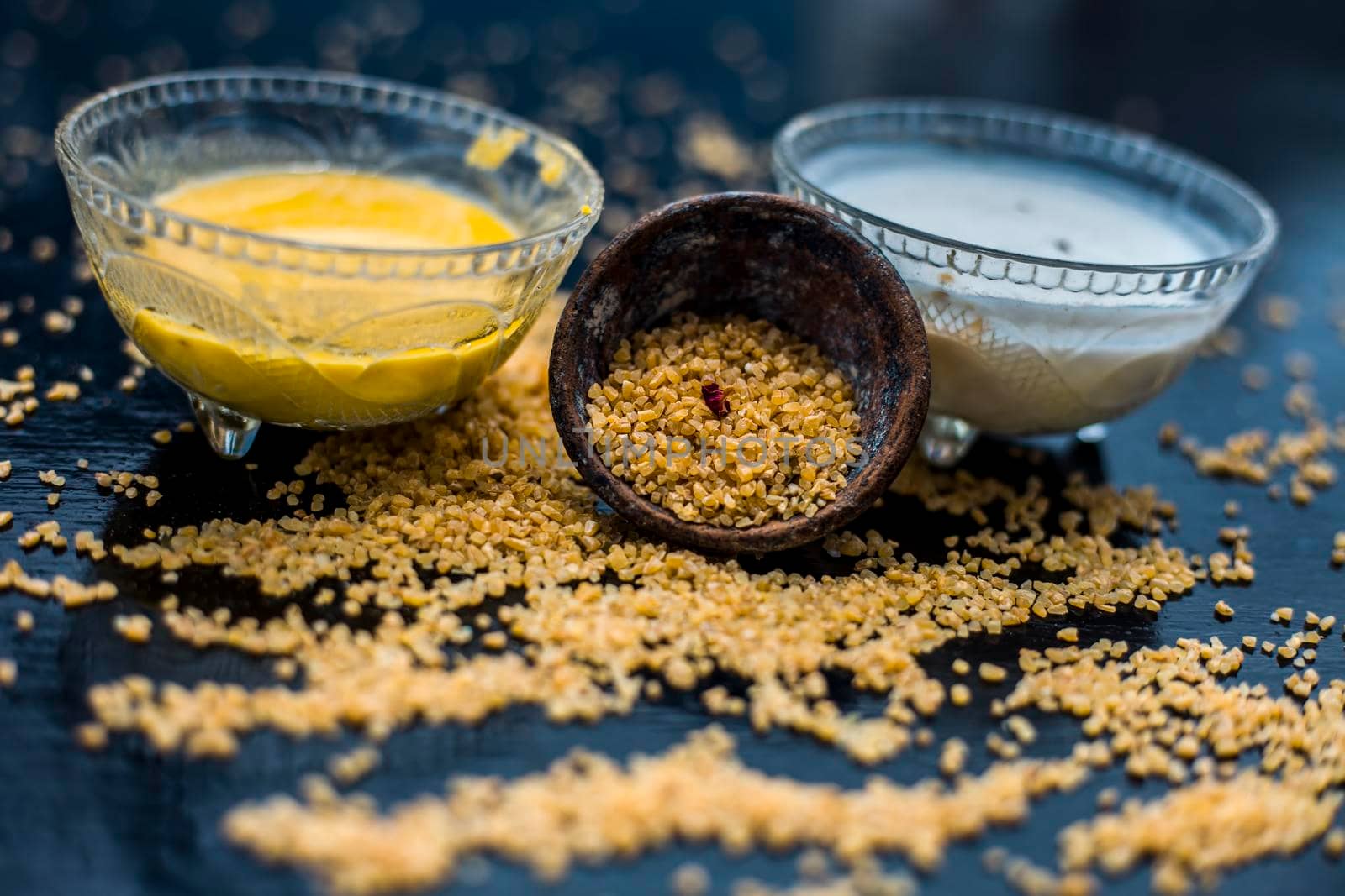 Curd or yogurt and oats face mask on the woodne surface in a glass bowl along with some raw oats in a black colored clay bowl and some spread on the surface. To Exfoliate Your Skin.