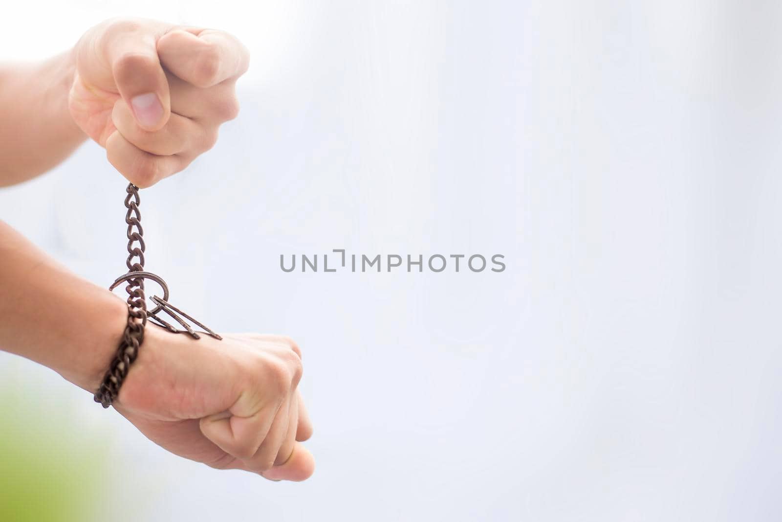 Close up of two hands one tied with a rusted chain and other pulling it shot with blurred background.