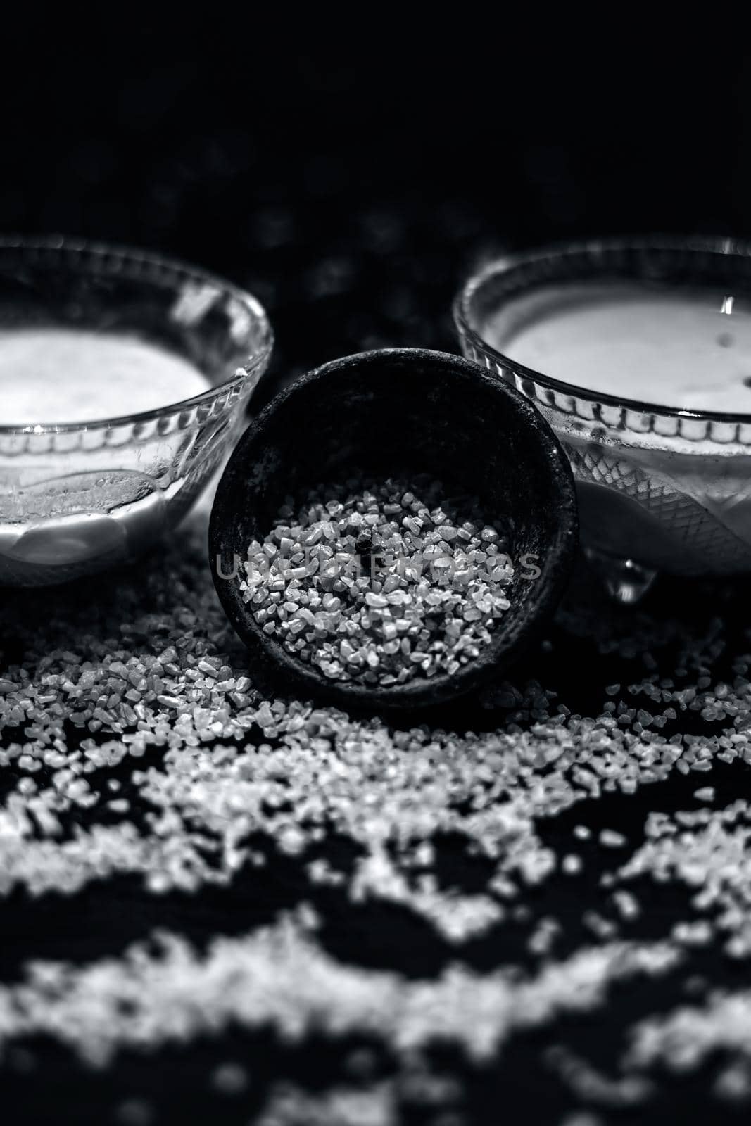 Curd or yogurt and oats face mask on the woodne surface in a glass bowl along with some raw oats in a black colored clay bowl and some spread on the surface. To Exfoliate Your Skin. by mirzamlk