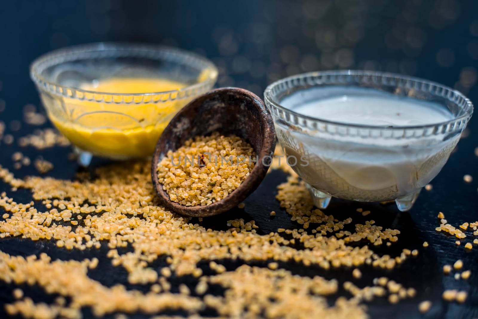 Curd or yogurt and oats face mask on the woodne surface in a glass bowl along with some raw oats in a black colored clay bowl and some spread on the surface. To Exfoliate Your Skin.