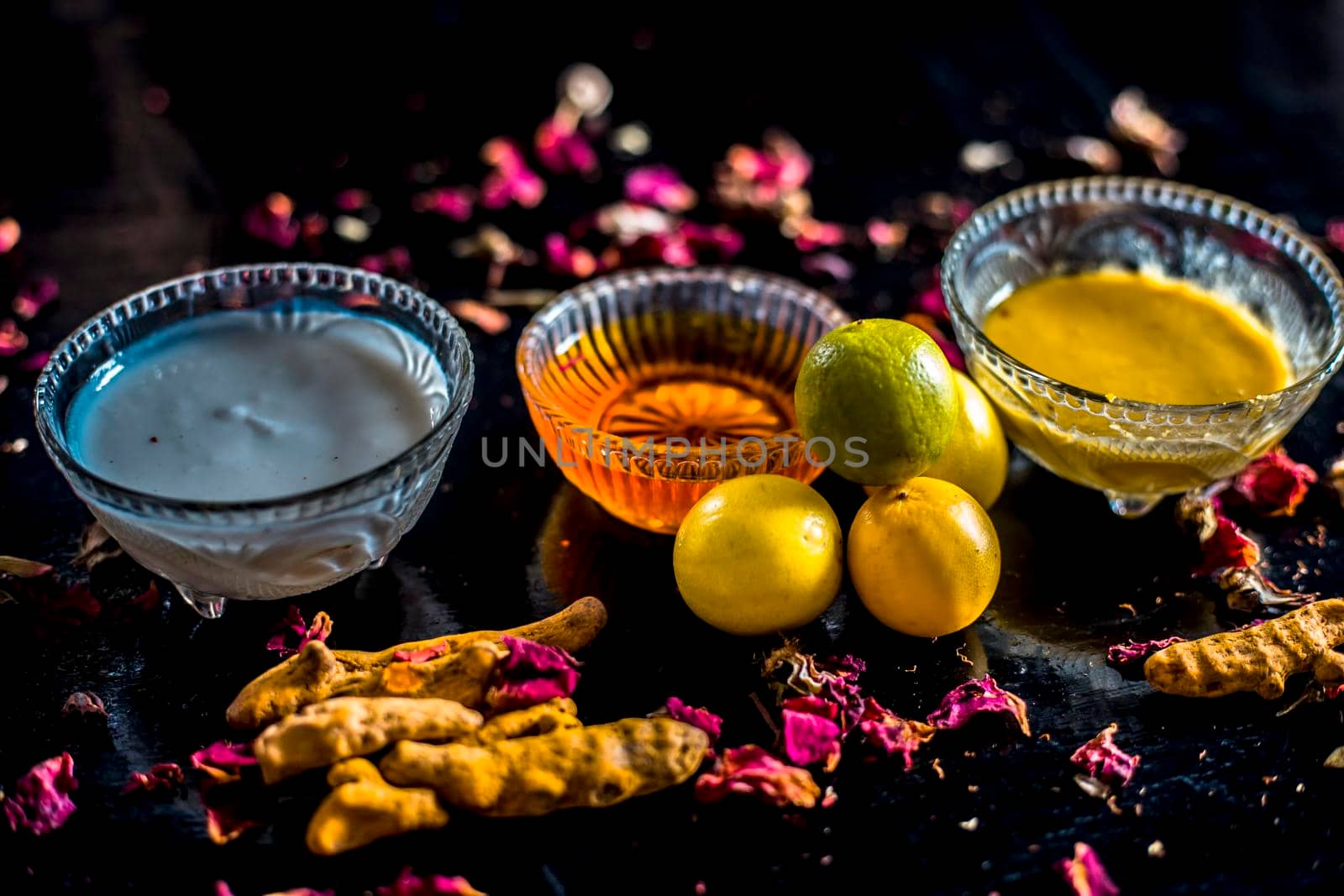 Face mask of lemon juice, honey, and curd along with some raw turmeric well mixed in a glass bowl along with entire raw ingredients on the wooden surface for acne-prone skin and blemishes.