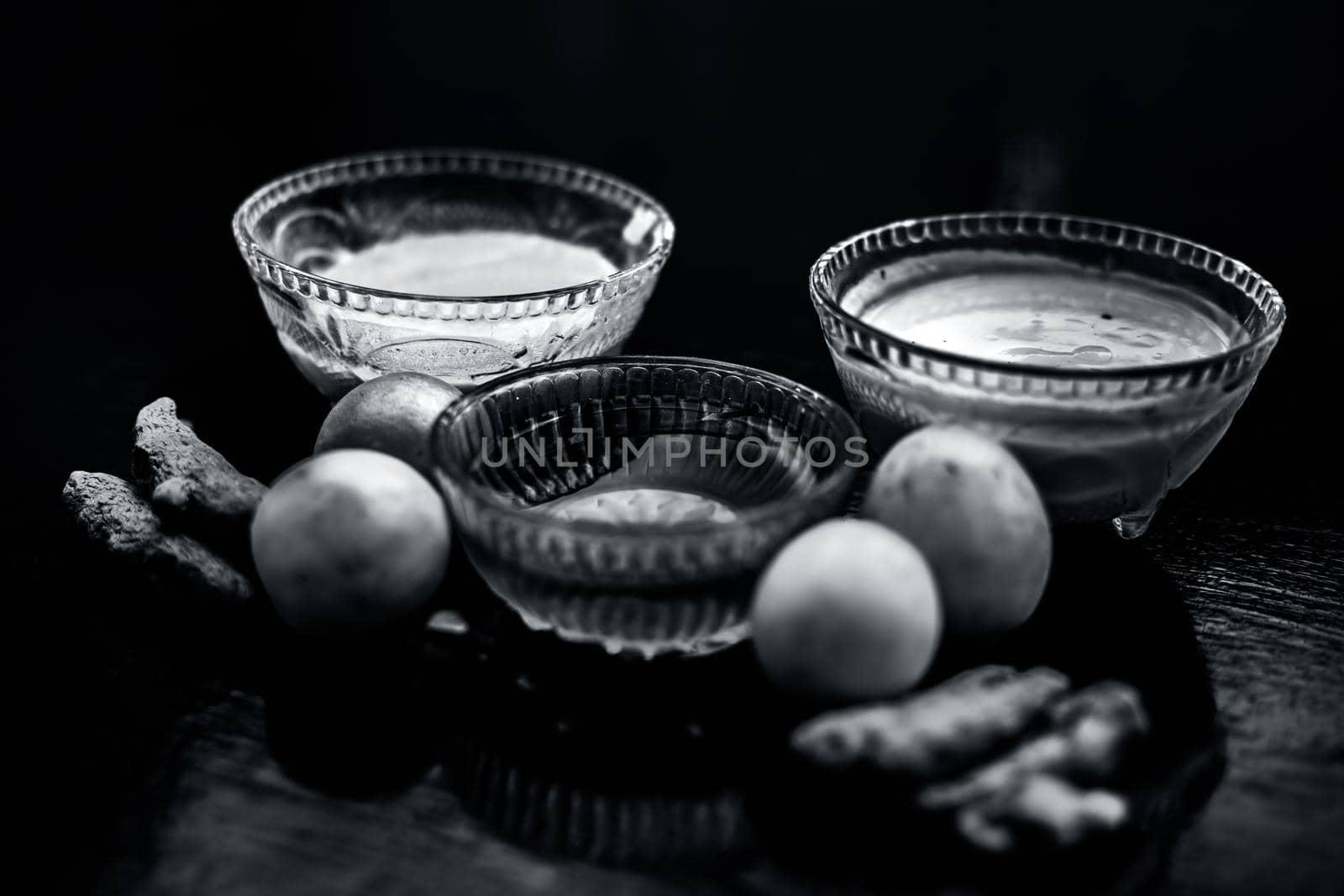 Face mask of lemon juice, honey, and curd along with some raw turmeric well mixed in a glass bowl along with entire raw ingredients on the wooden surface for acne-prone skin and blemishes.