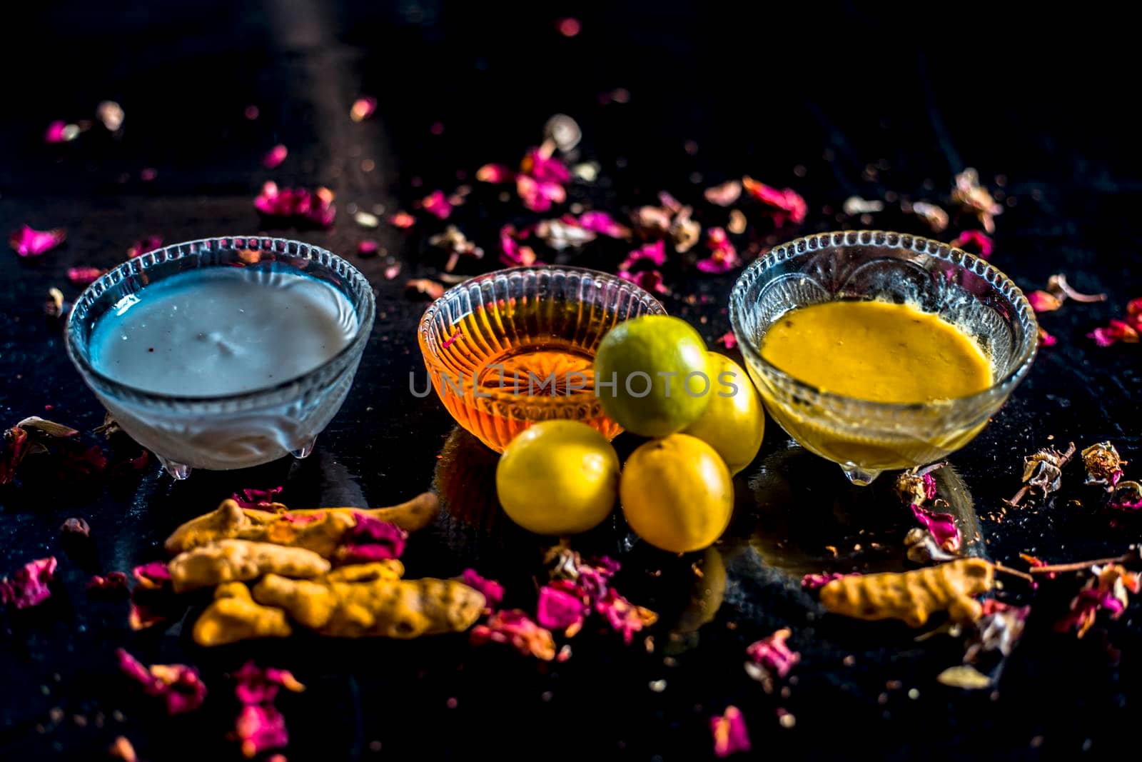 Face mask of lemon juice, honey, and curd along with some raw turmeric well mixed in a glass bowl along with entire raw ingredients on the wooden surface for acne-prone skin and blemishes.