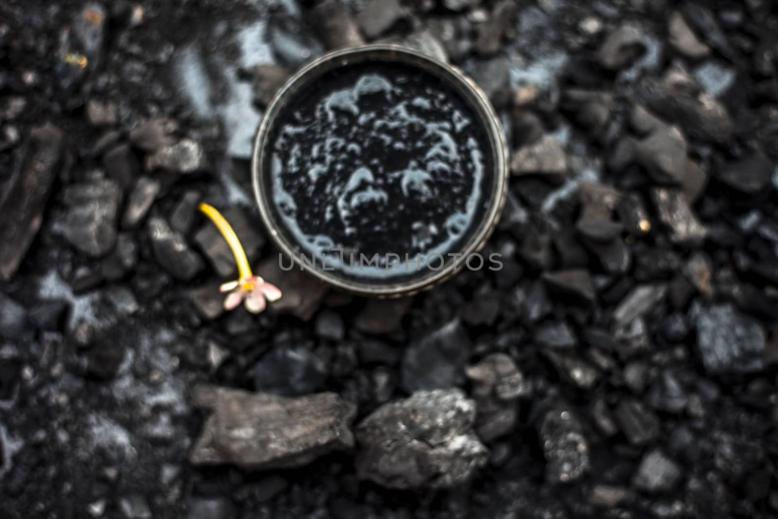 Close up of activated charcoal in a glass bowl on the wooden surface along with some raw powder of charcoal or coal spread on the surface. by mirzamlk