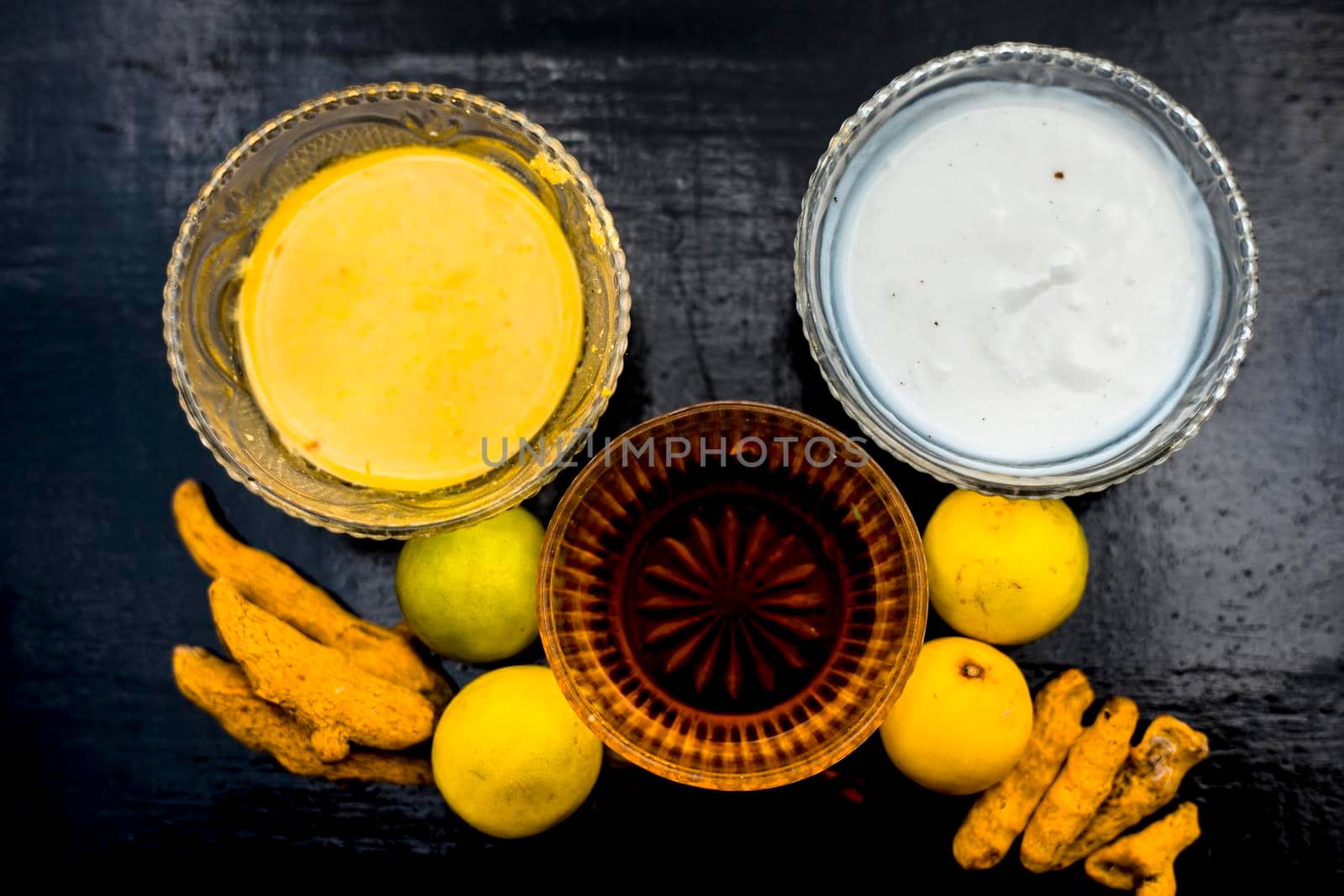 Face mask of lemon juice, honey, and curd along with some raw turmeric well mixed in a glass bowl along with entire raw ingredients on the wooden surface for acne-prone skin and blemishes.