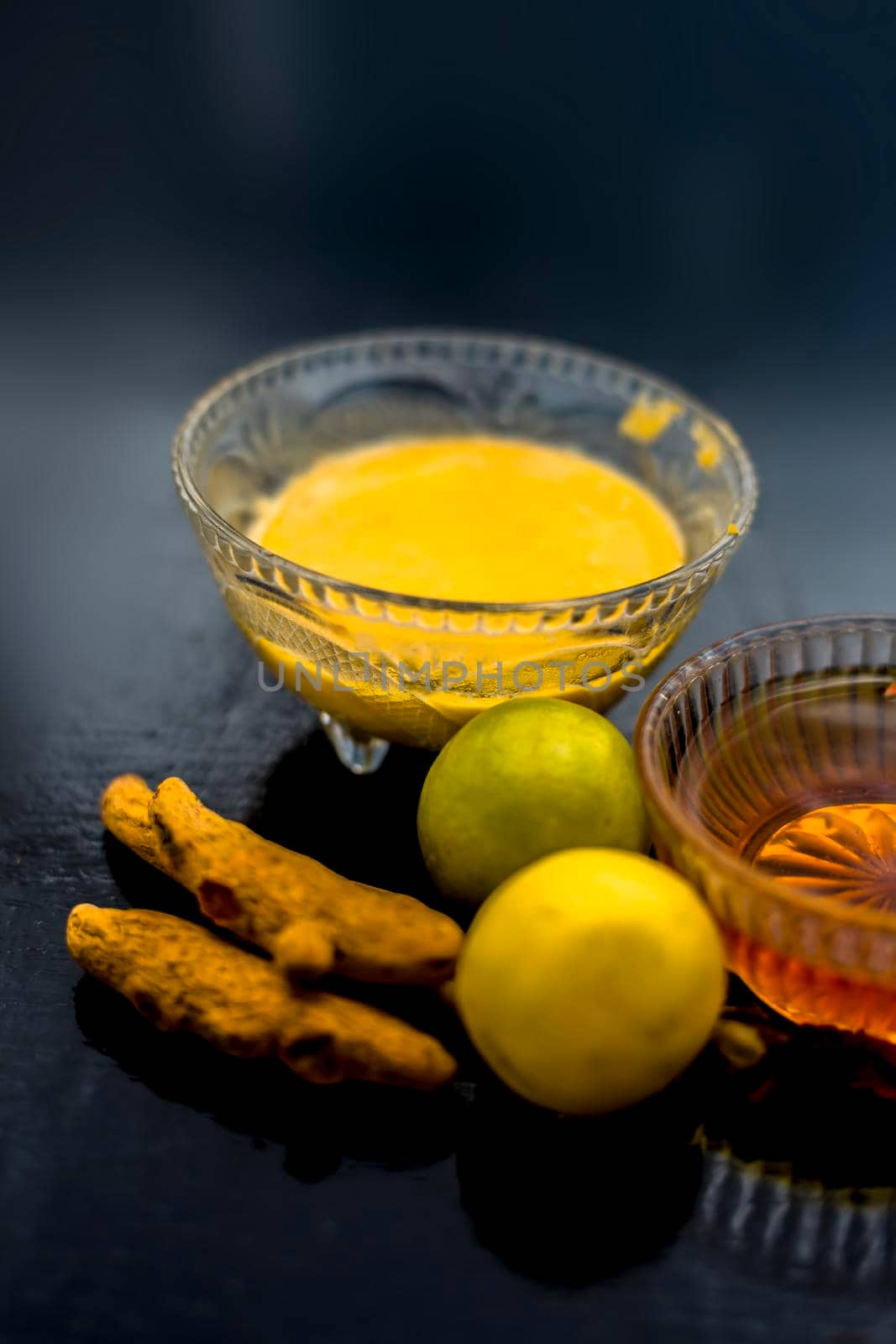 Face mask of lemon juice, honey, and curd along with some raw turmeric well mixed in a glass bowl along with entire raw ingredients on the wooden surface for acne-prone skin and blemishes.