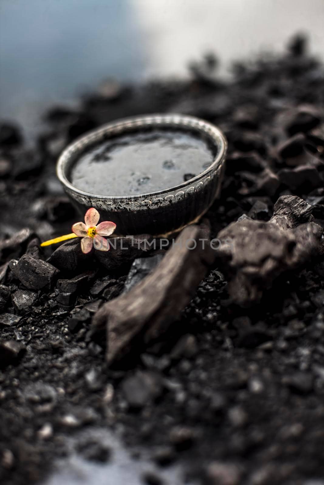 Close up of activated charcoal in a glass bowl on the wooden surface along with some raw powder of charcoal or coal spread on the surface. by mirzamlk