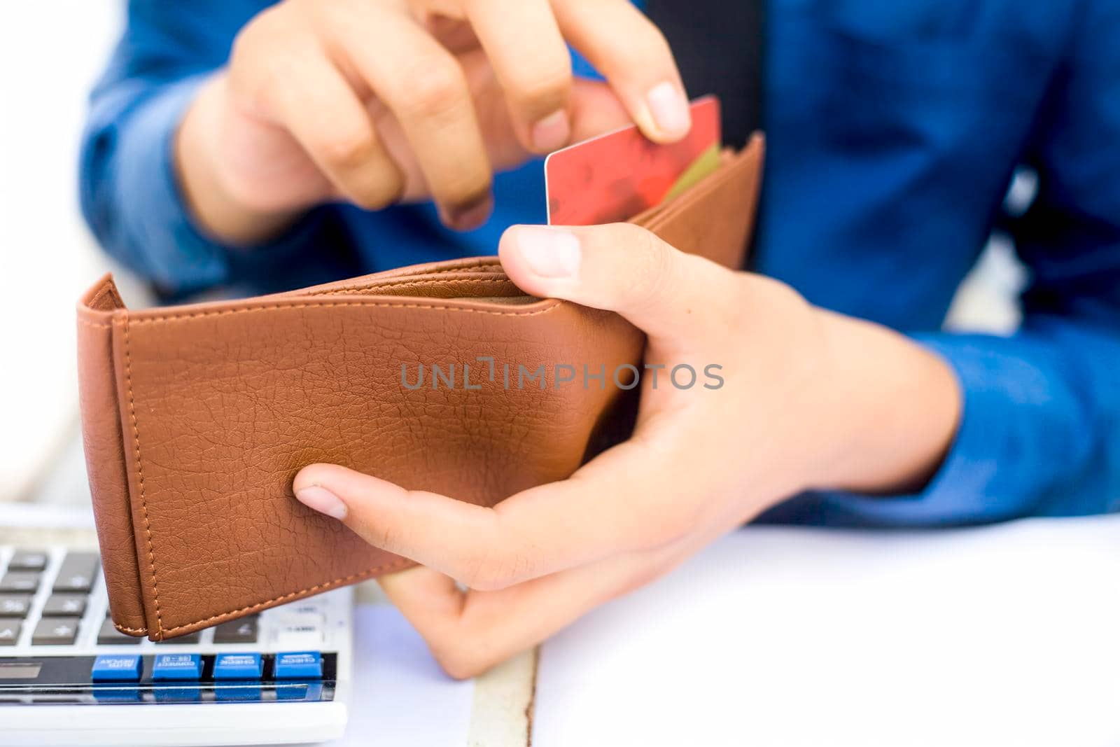 Businessman wearing a dark blue colored shirt with black tie and taking out his credit card from his brown colored wallet isolated on white.