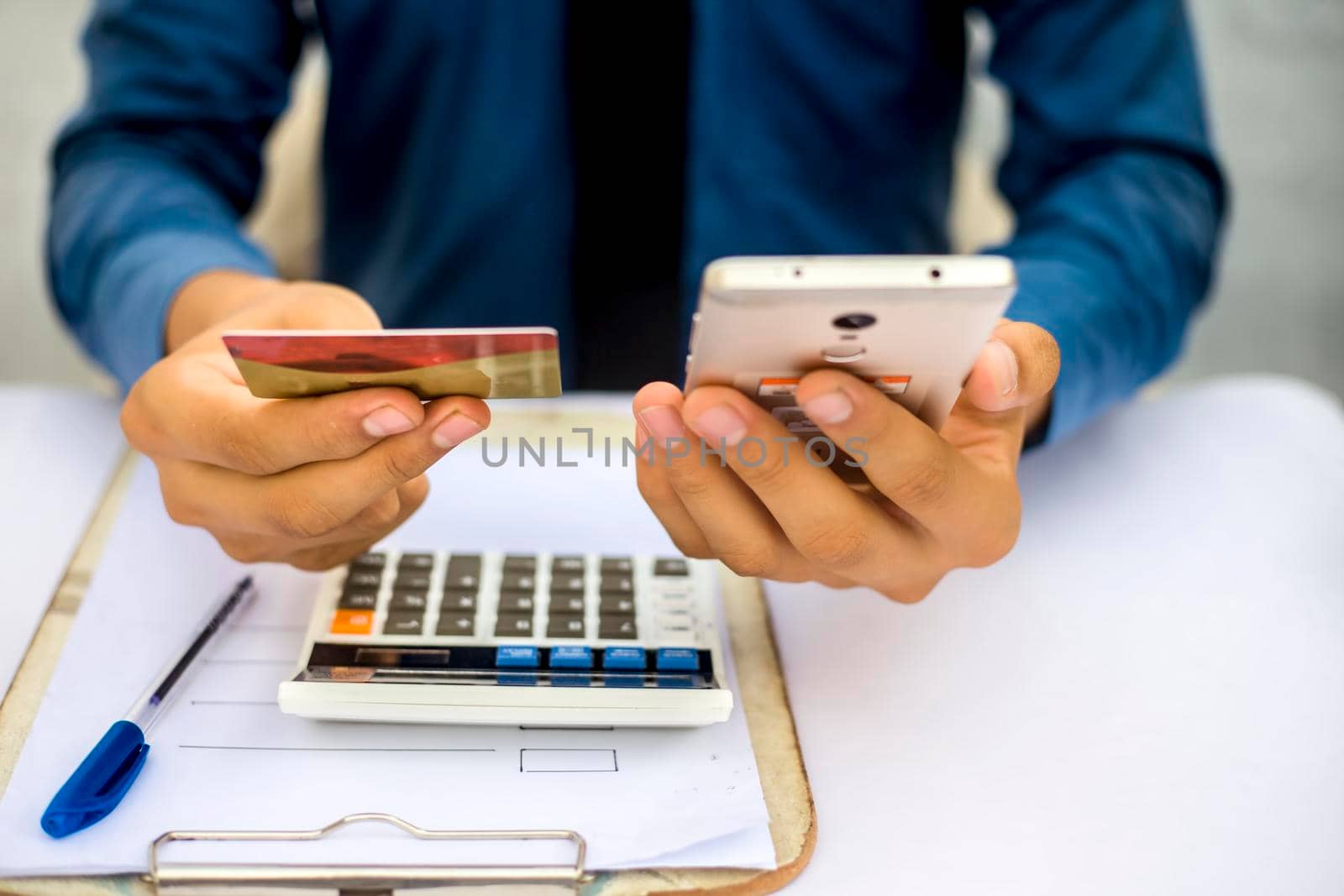 Close up of employee holding a smart cell phone and credit card in his hand wearing a blue colored shirt and black necktie. Concept of banking and shopping isolated on white. by mirzamlk