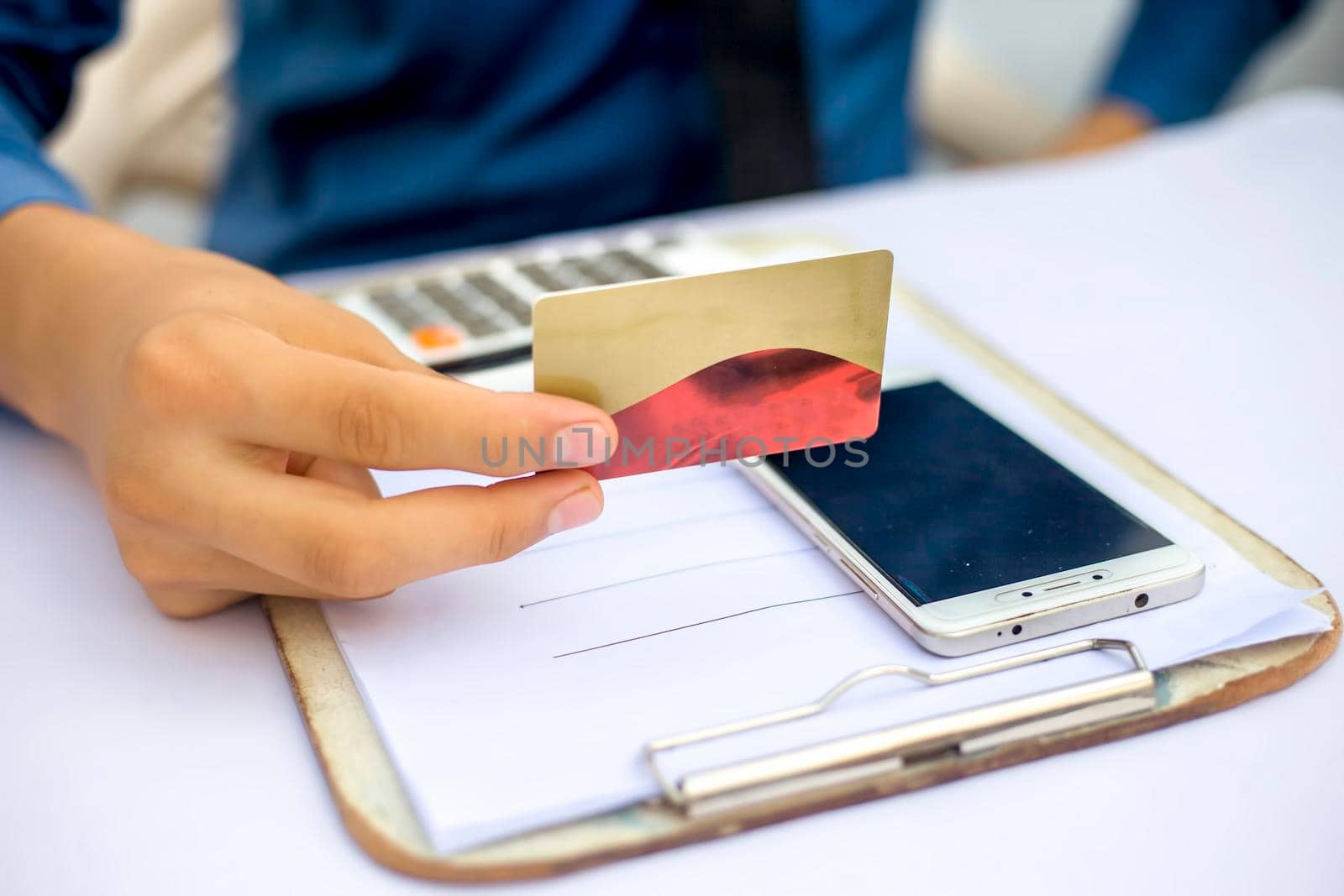 Close up of employee holding a smart cell phone and credit card in his hand wearing a blue colored shirt and black necktie. Concept of banking and shopping isolated on white. by mirzamlk