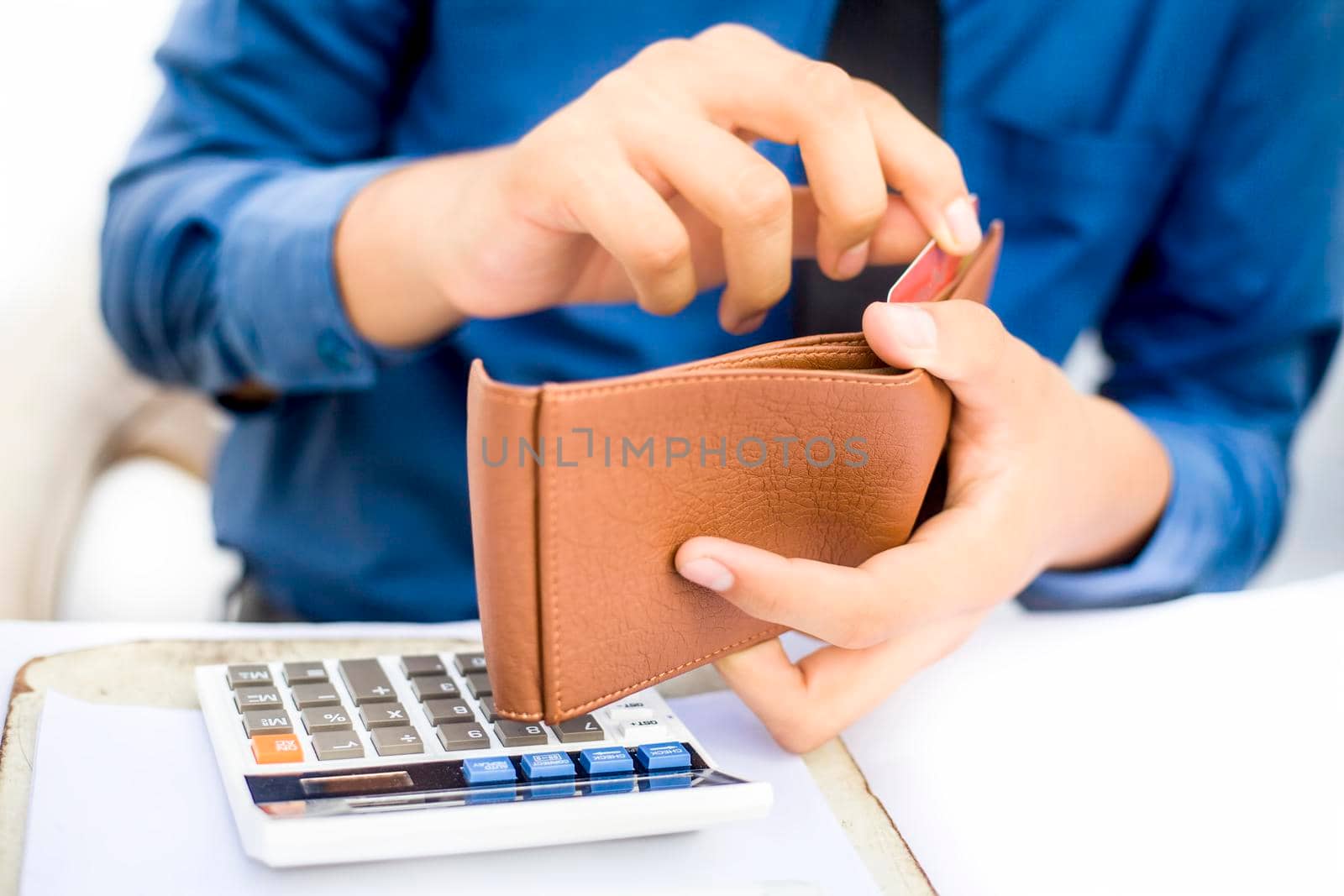 Businessman wearing a dark blue colored shirt with black tie and taking out his credit card from his brown colored wallet isolated on white. by mirzamlk