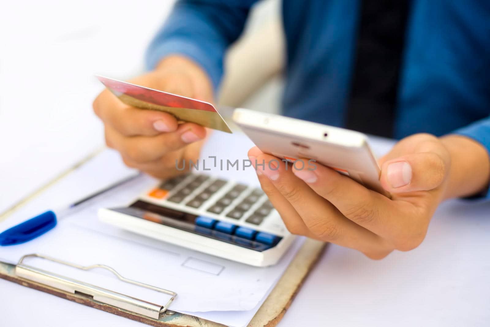 Close up of employee holding a smart cell phone and credit card in his hand wearing a blue colored shirt and black necktie. Concept of banking and shopping isolated on white.
