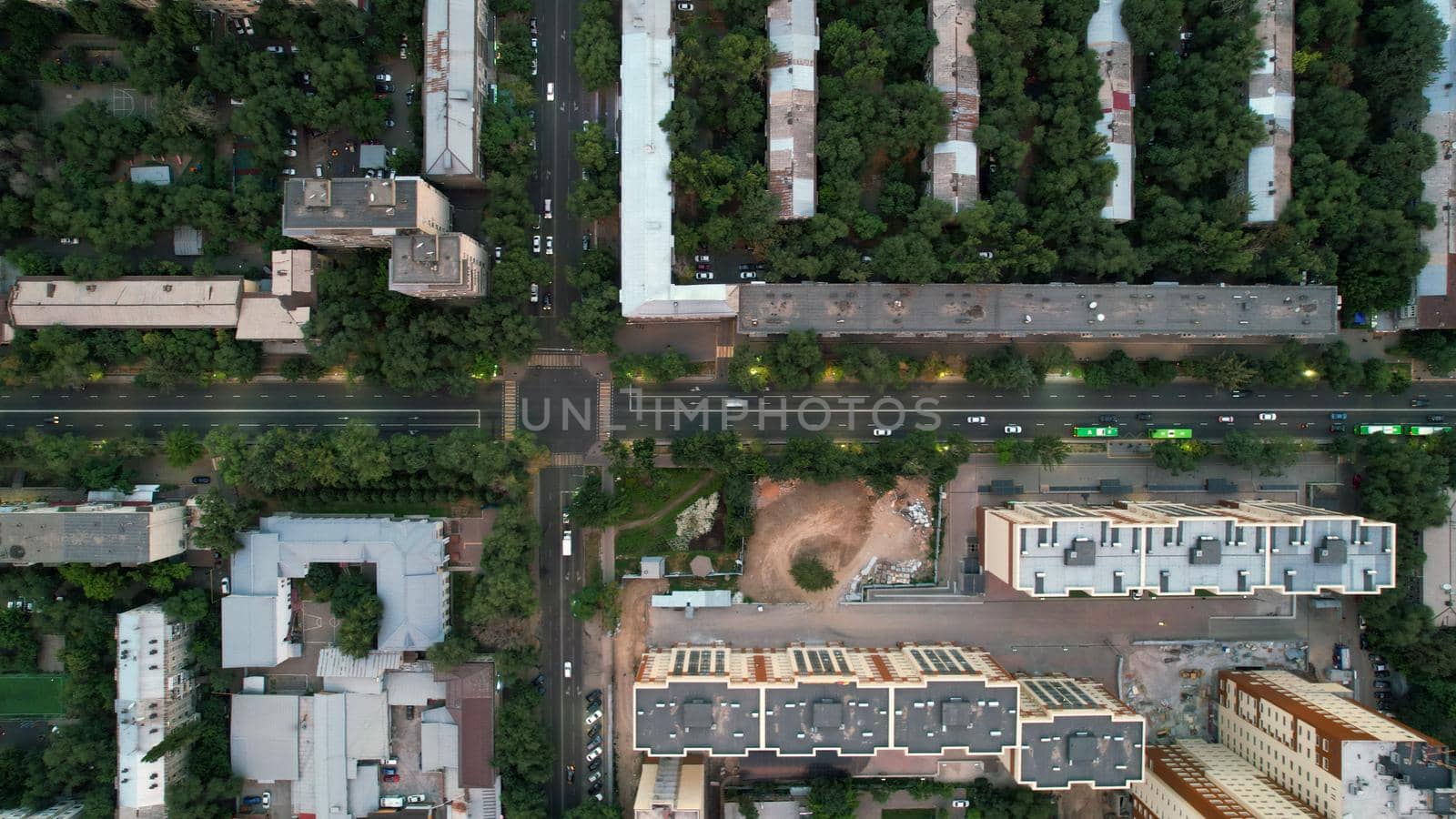 Top view from a drone on the central road of Almaty. Trees are growing in all courtyards, new houses are being built. Rides different cars and buses. There are cars at the intersection. Kazakhstan