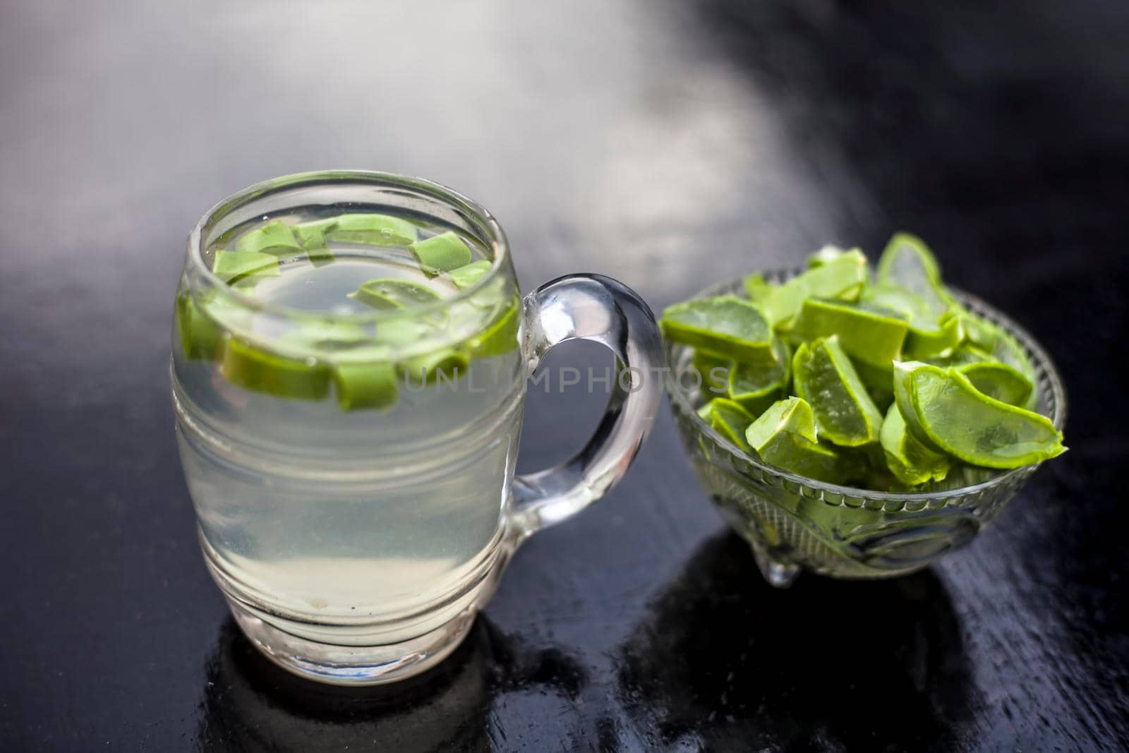 Close up of glass mug on wooden surface containing aloe vera detox drink in along with its entire raw ingredients with it. Horizontal shot with blurred background. by mirzamlk