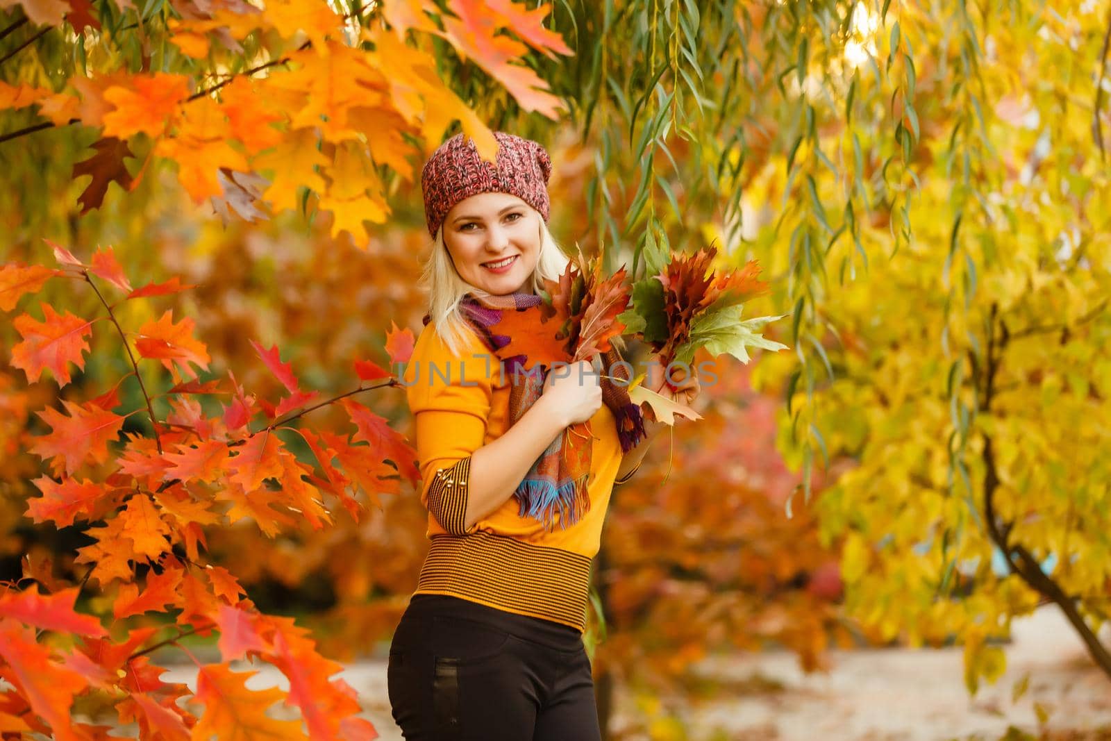 Fashion woman in autumn park holding yellow leaf