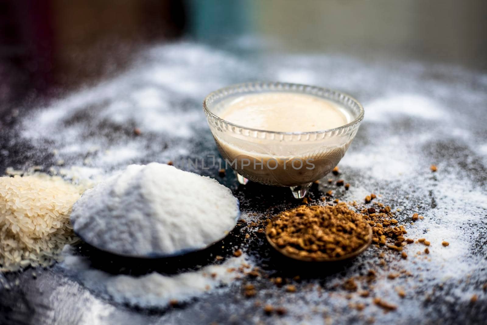 Hair growth remedy of rice flour water and fenugreek/coriander/parsley seeds powder on wooden surface and its paste in a glass bowl with some rice flour spread on the surface. Horizontal shot.