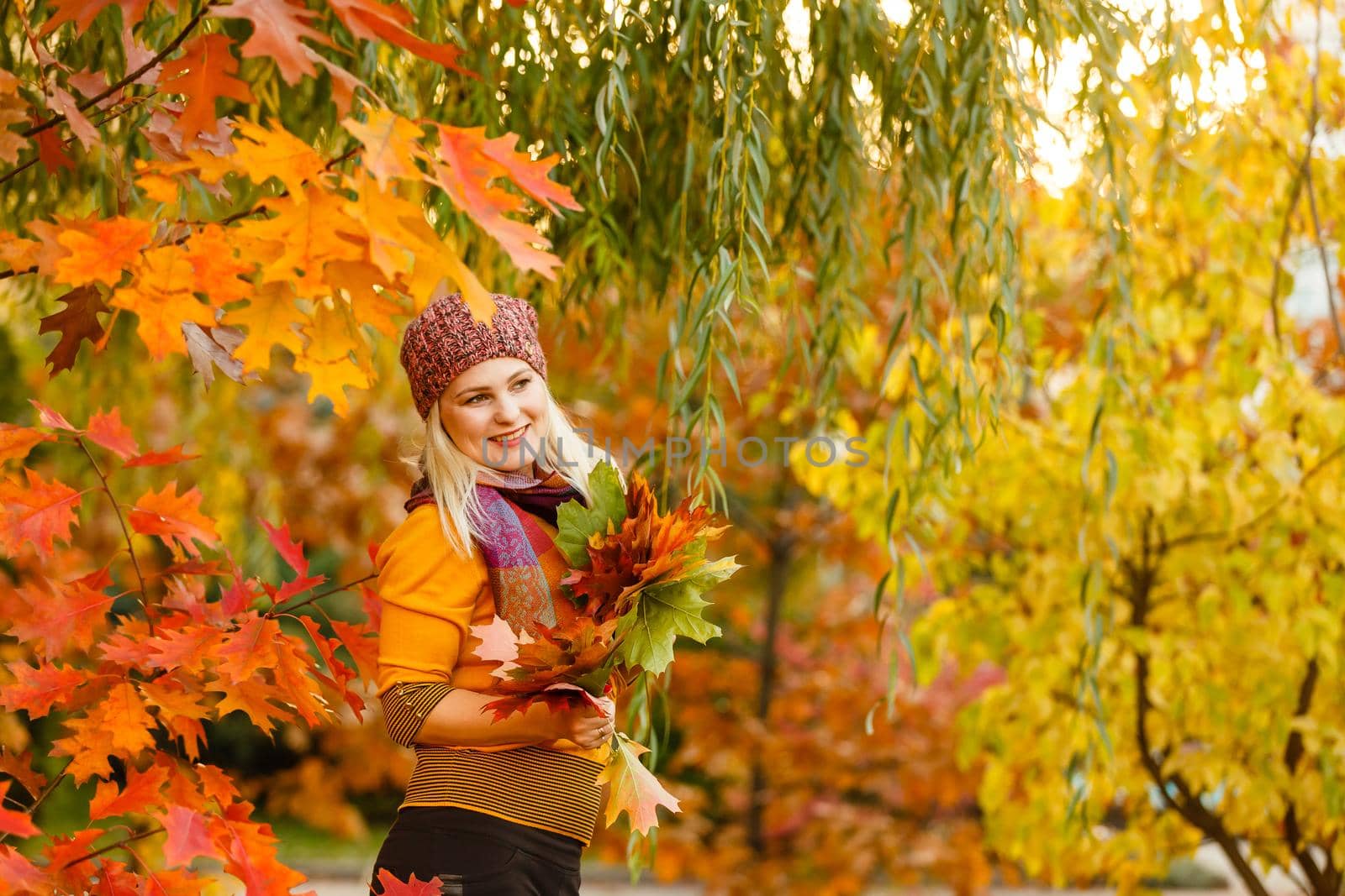 Young woman with autumn leaves in hand and fall yellow maple garden background