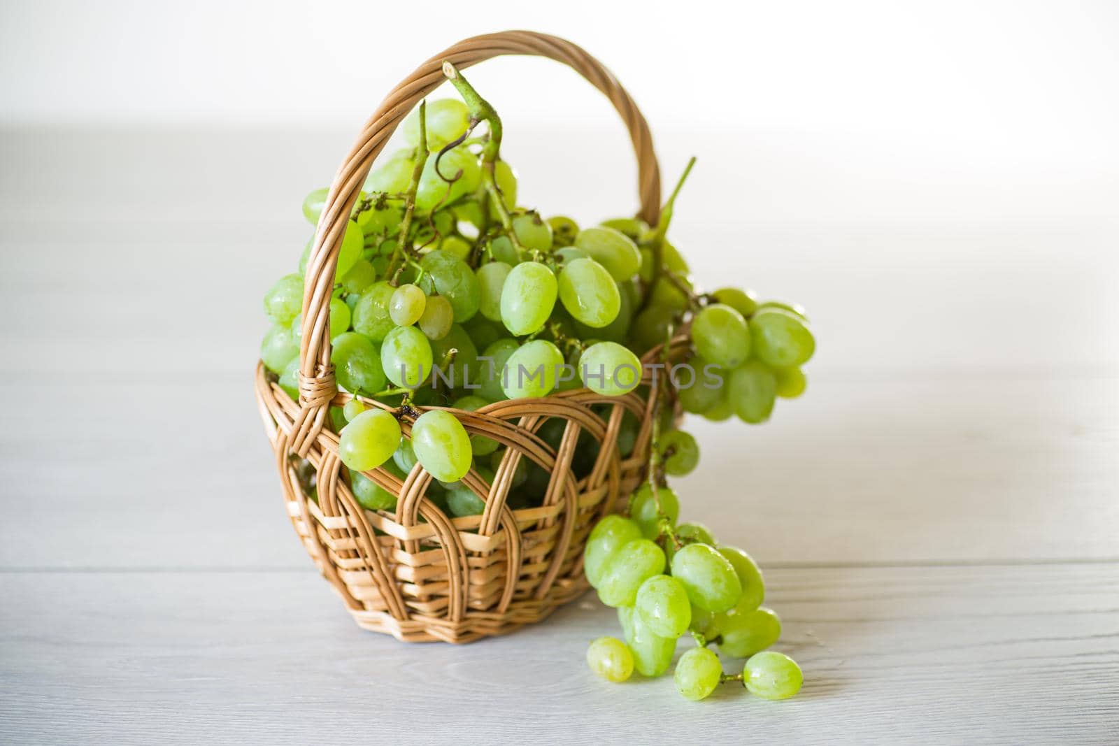green autumn ripe grapes in a basket on a light wooden table