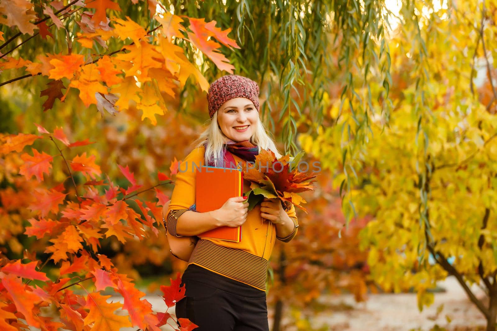 Young woman with autumn leaves in hand and fall yellow maple garden background