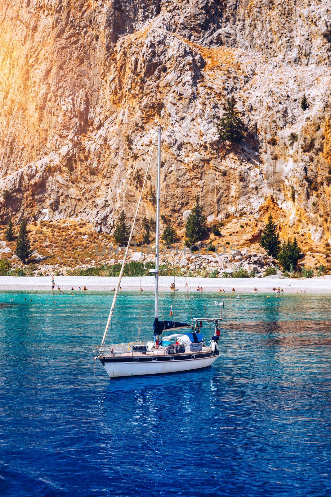 Yacht anchoring in crystal clear turquoise water in front of the tropical island, alternative lifestyle, living on a boat. View of yacht at anchor on turquoise water, showing luxury, wealth.