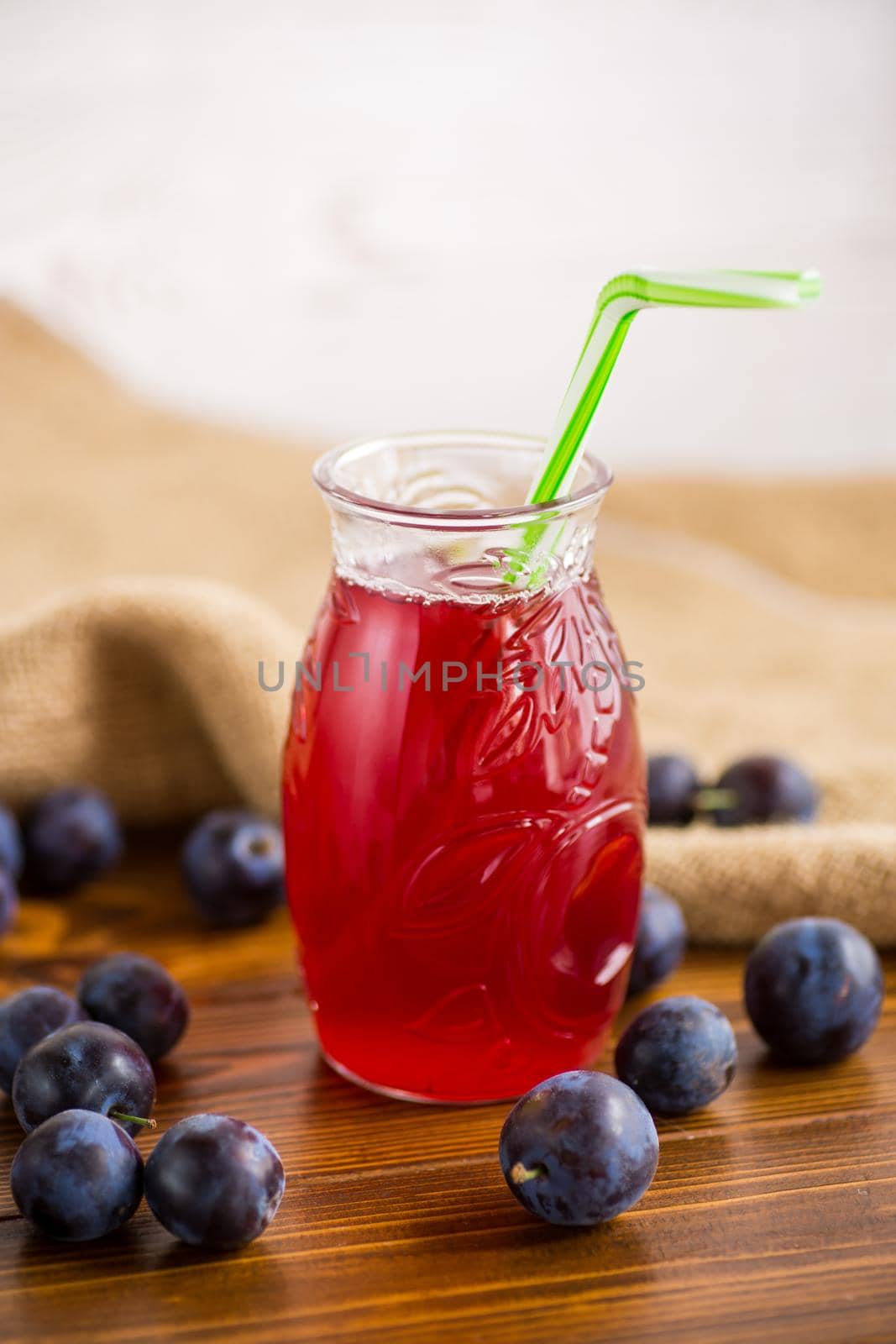 Sweet natural plum drink in a glass with a straw on a wooden table