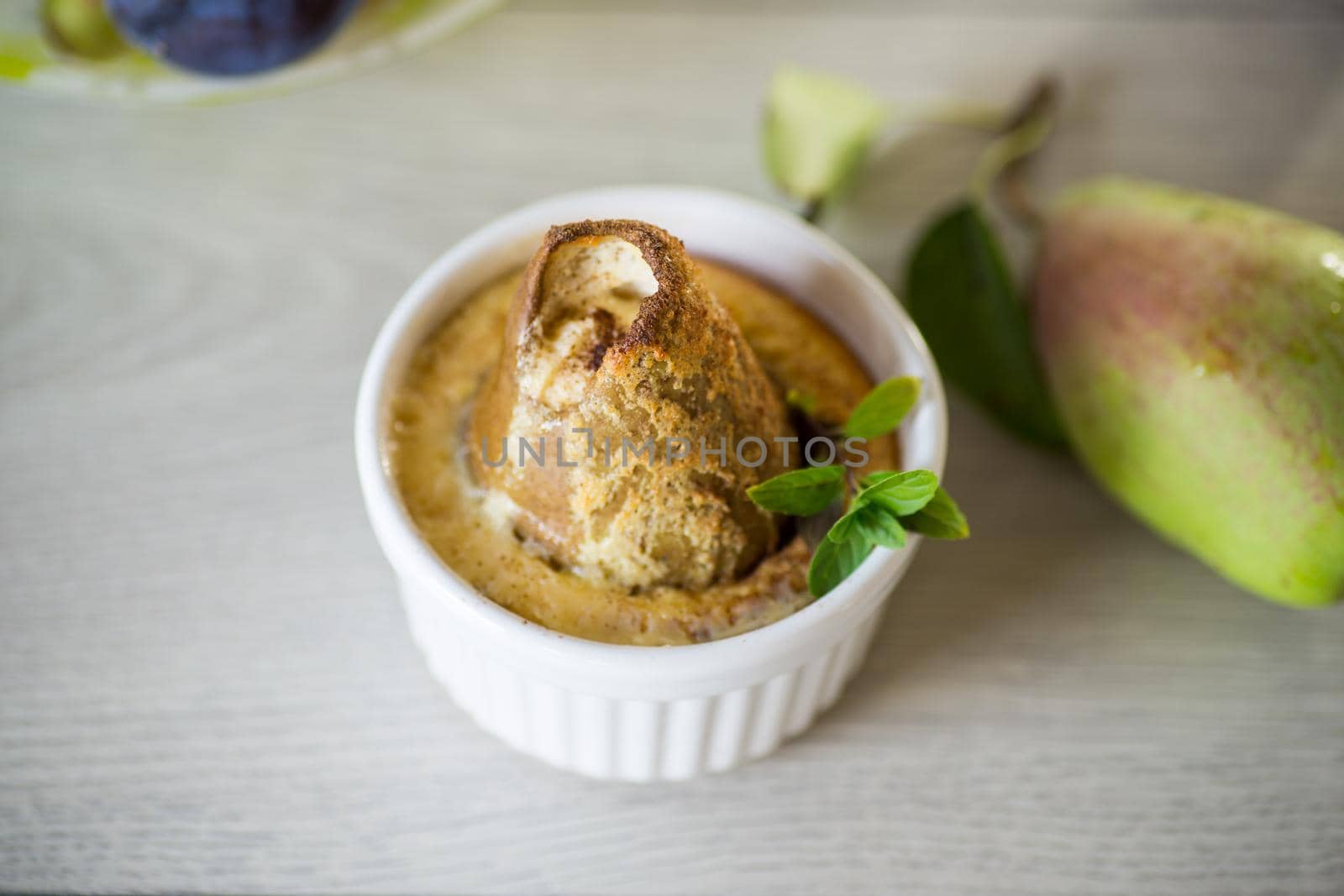 pear baked in curd dough in a small ceramic form, on a wooden table.