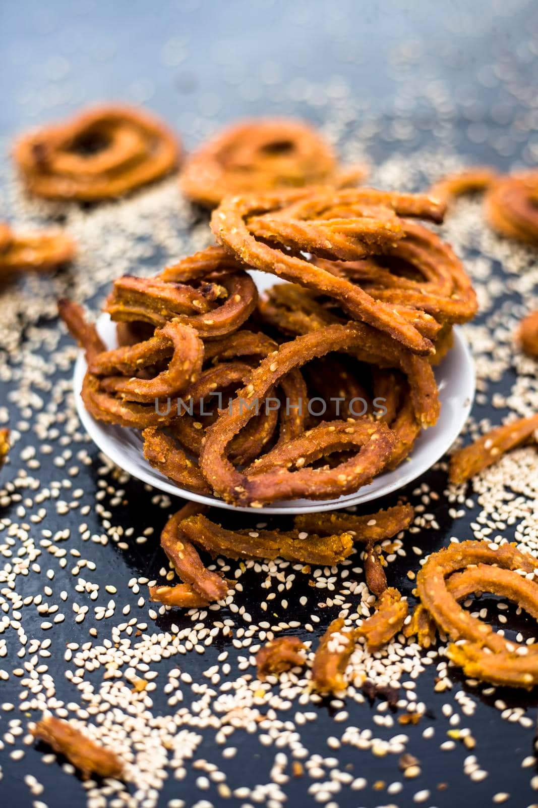 Famous Indian snack in a glass plate on the wooden surface along with raw sesame seeds or til spread on the surface.