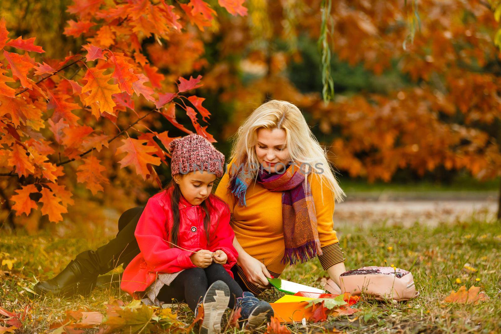 Happy mother met her kid daughter after classes. Child reading books outdoors primary school. by Andelov13