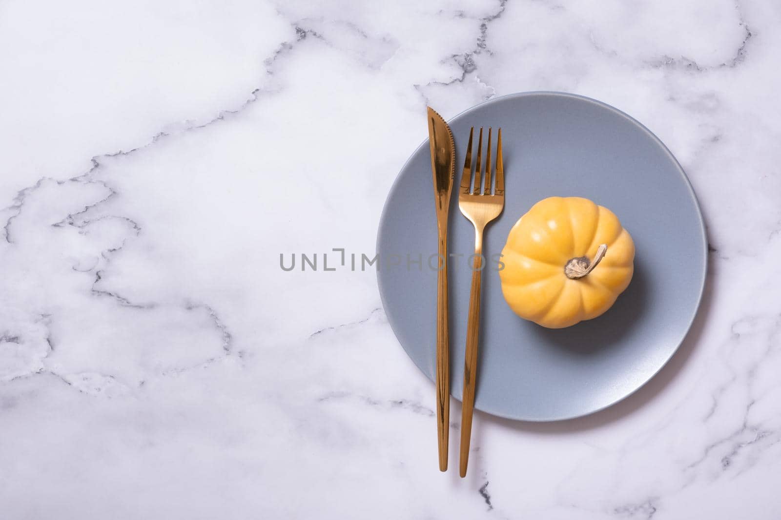 Orange pumpkin on a blue plate with cutlery. Minimalist concept of the autumn menu by ssvimaliss