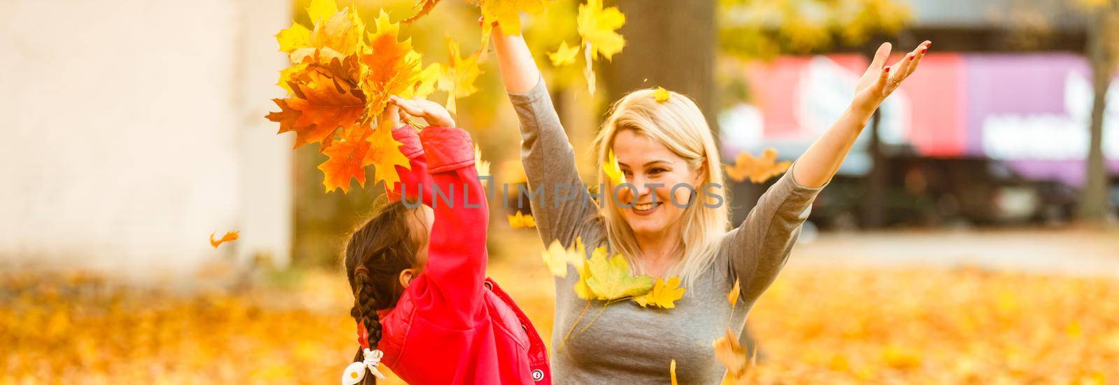 Happy parent and kid holding autumn yellow leaves outdoor.