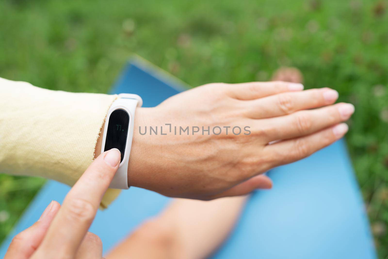 Sports girl doing stretching in nature outdoors, the girl looks at her fitness bracelet and checks her breathing during exercise. A woman is doing yoga in the park, sitting on the grass on a yoga mat