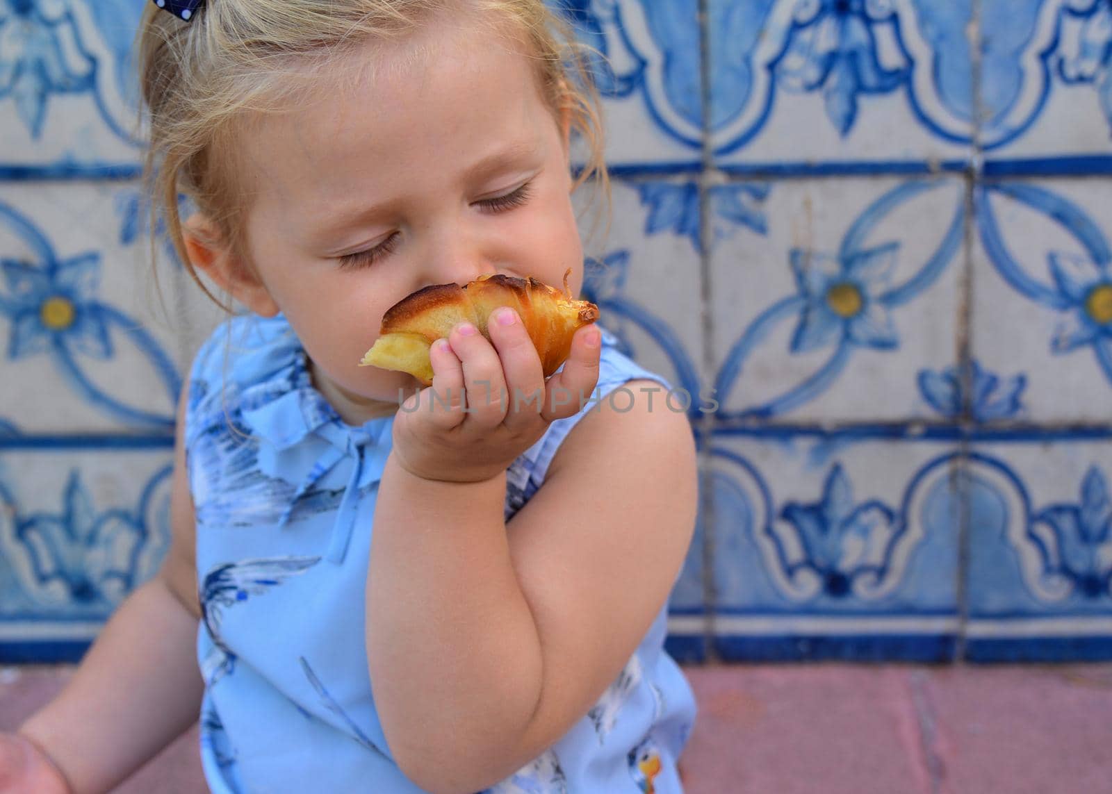 The girl is eating Pasteis de Belem egg tart. Azulejos tile on a background
