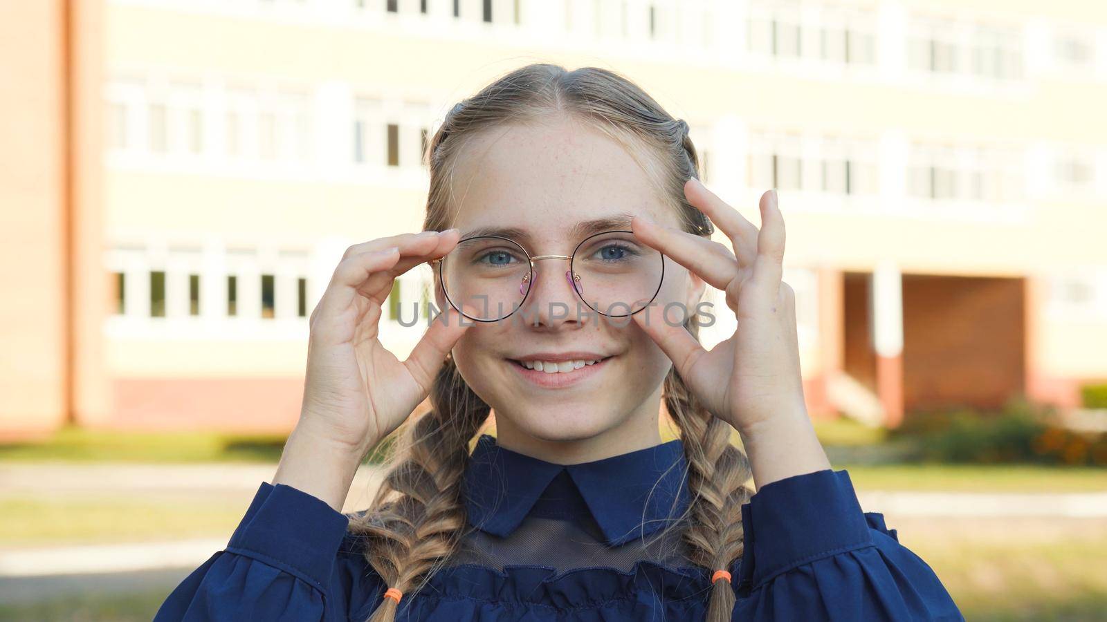 A teenage girl wearing glasses in front of a school