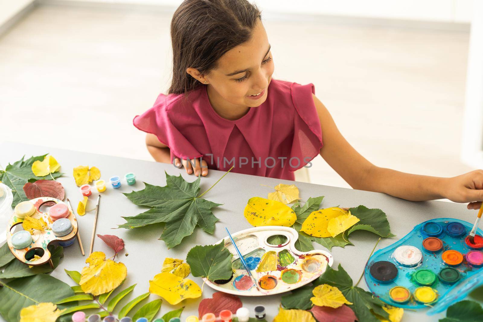 little girl artist with a brush and paints in her hands in autumn draws a landscape with leaves on canvas. High quality photo
