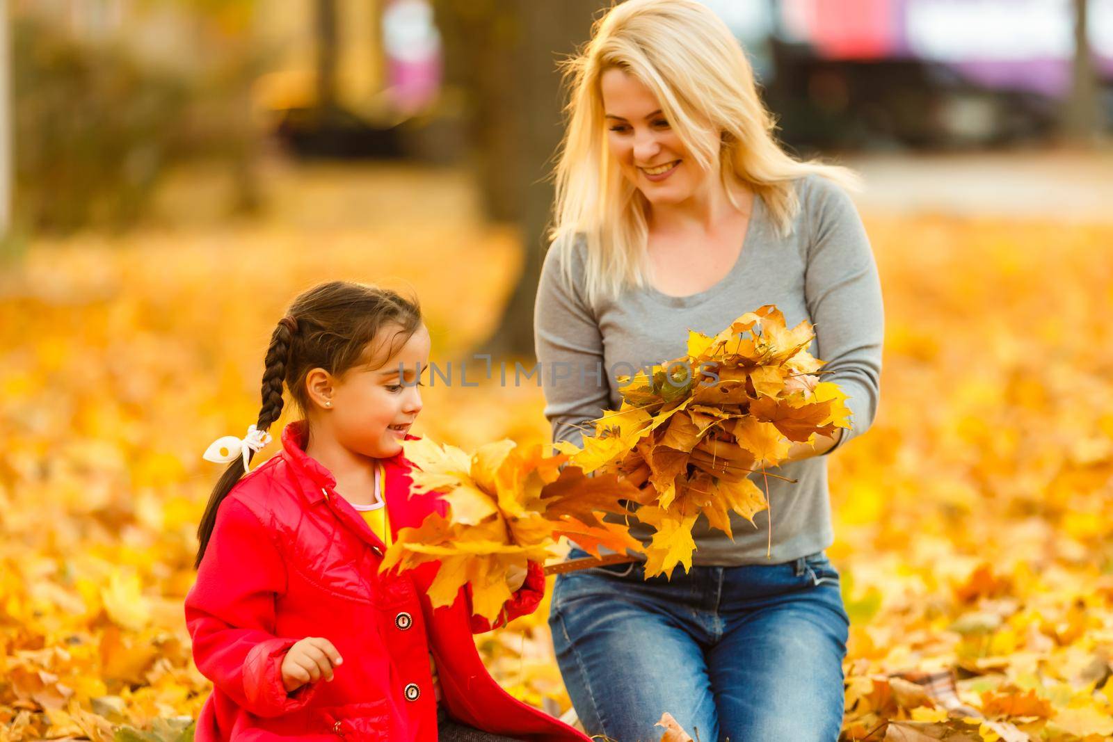 Happy parent and kid holding autumn yellow leaves outdoor. by Andelov13