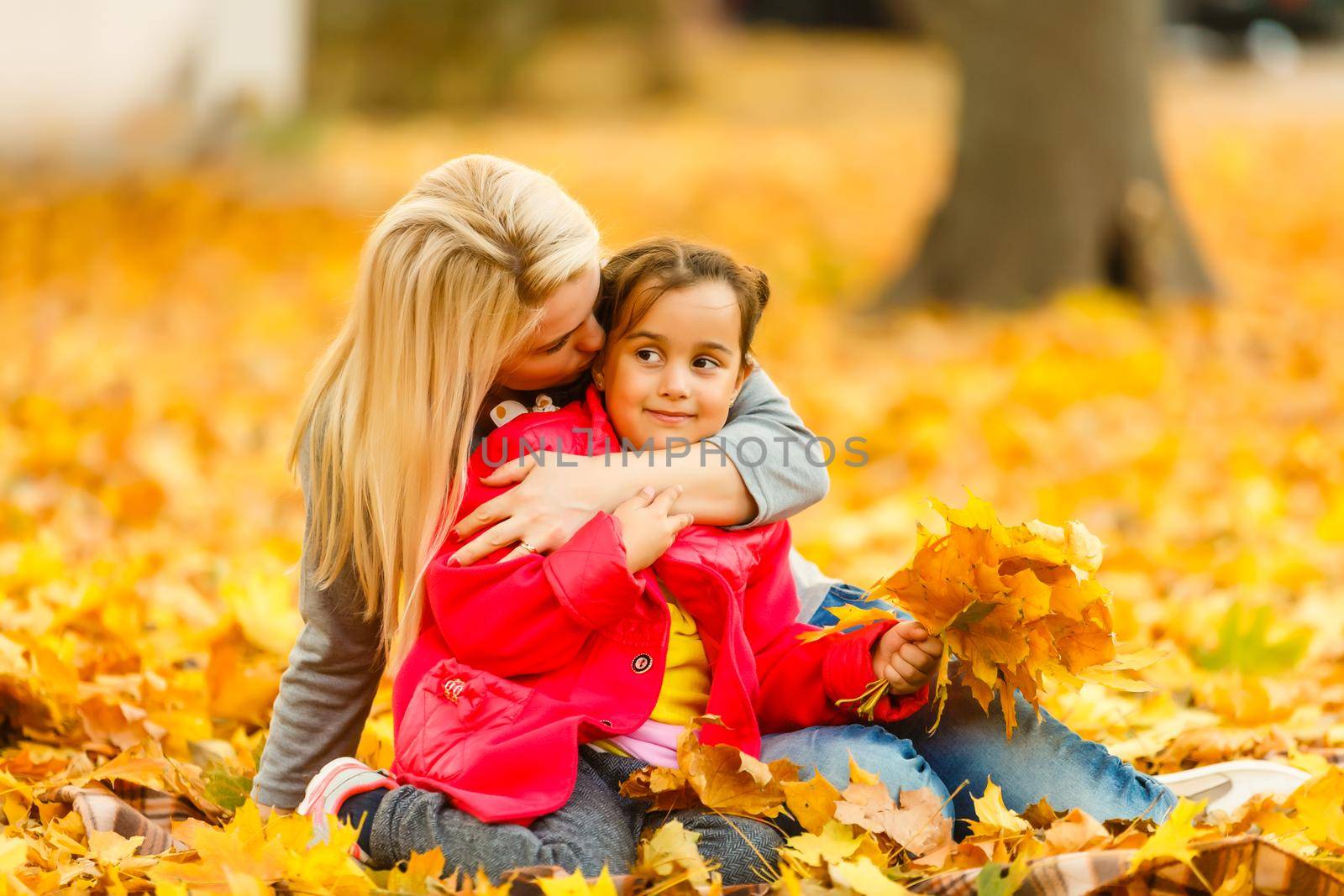 Happy parent and kid holding autumn yellow leaves outdoor.