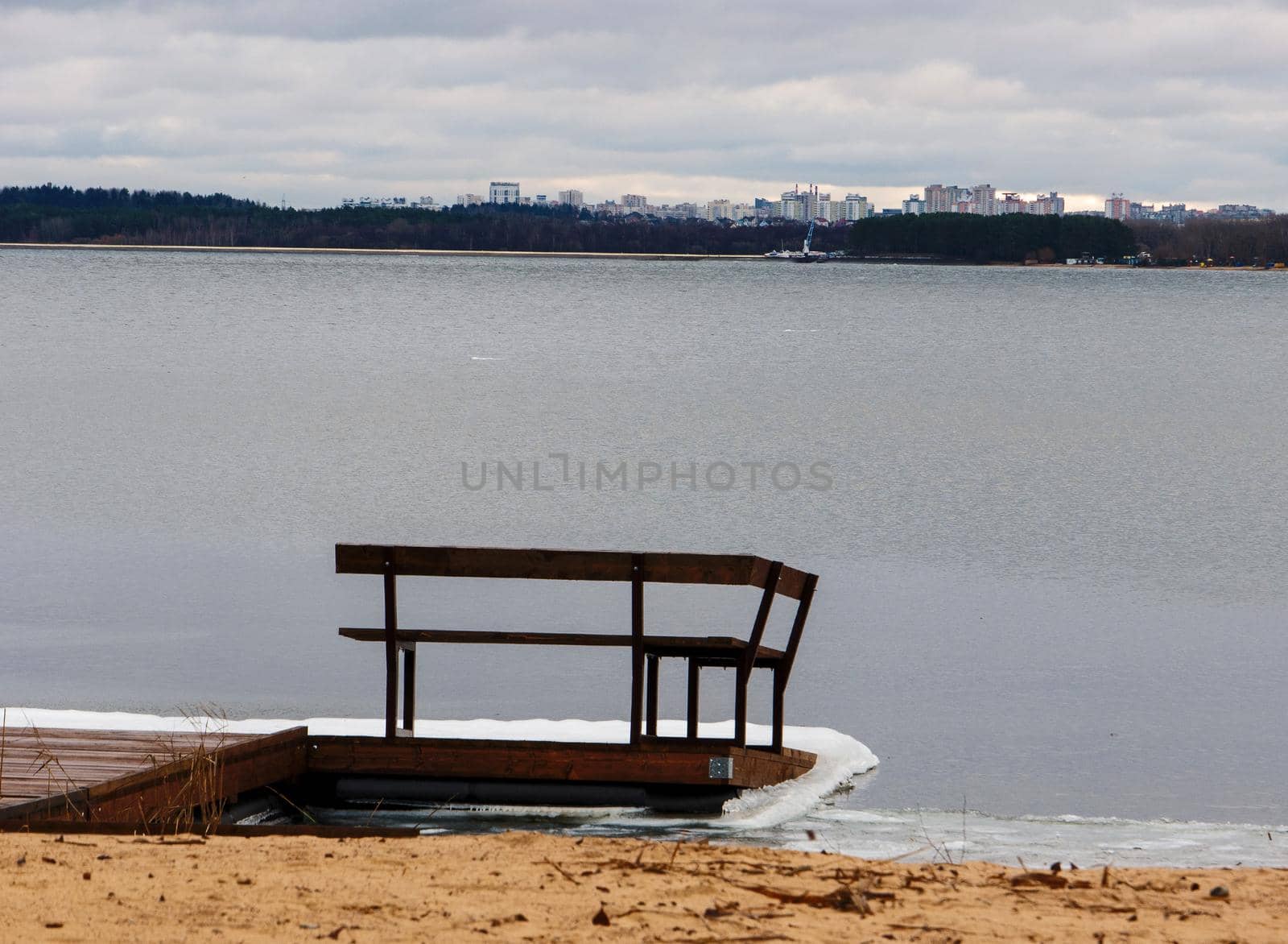 A small pier with a wooden bench on the shore of a winter lake. by gelog67