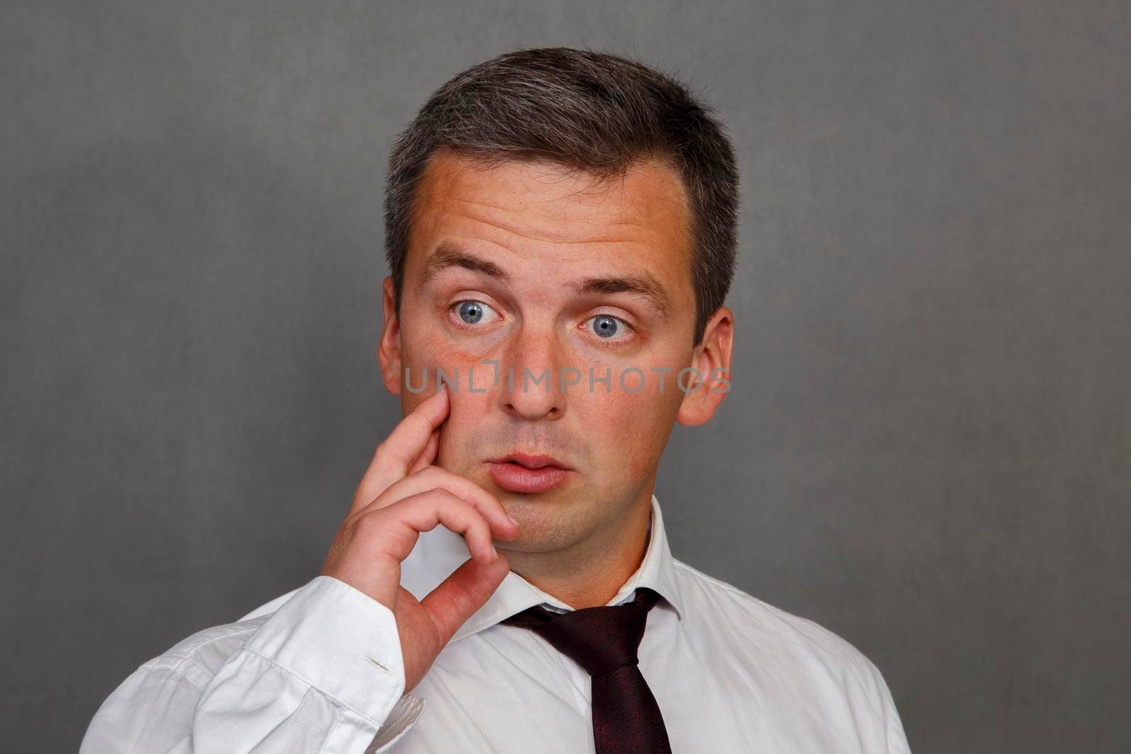 Crazy man 30-35 years old in white shirt with tie on gray background. Crazy guy. Negative emotion.