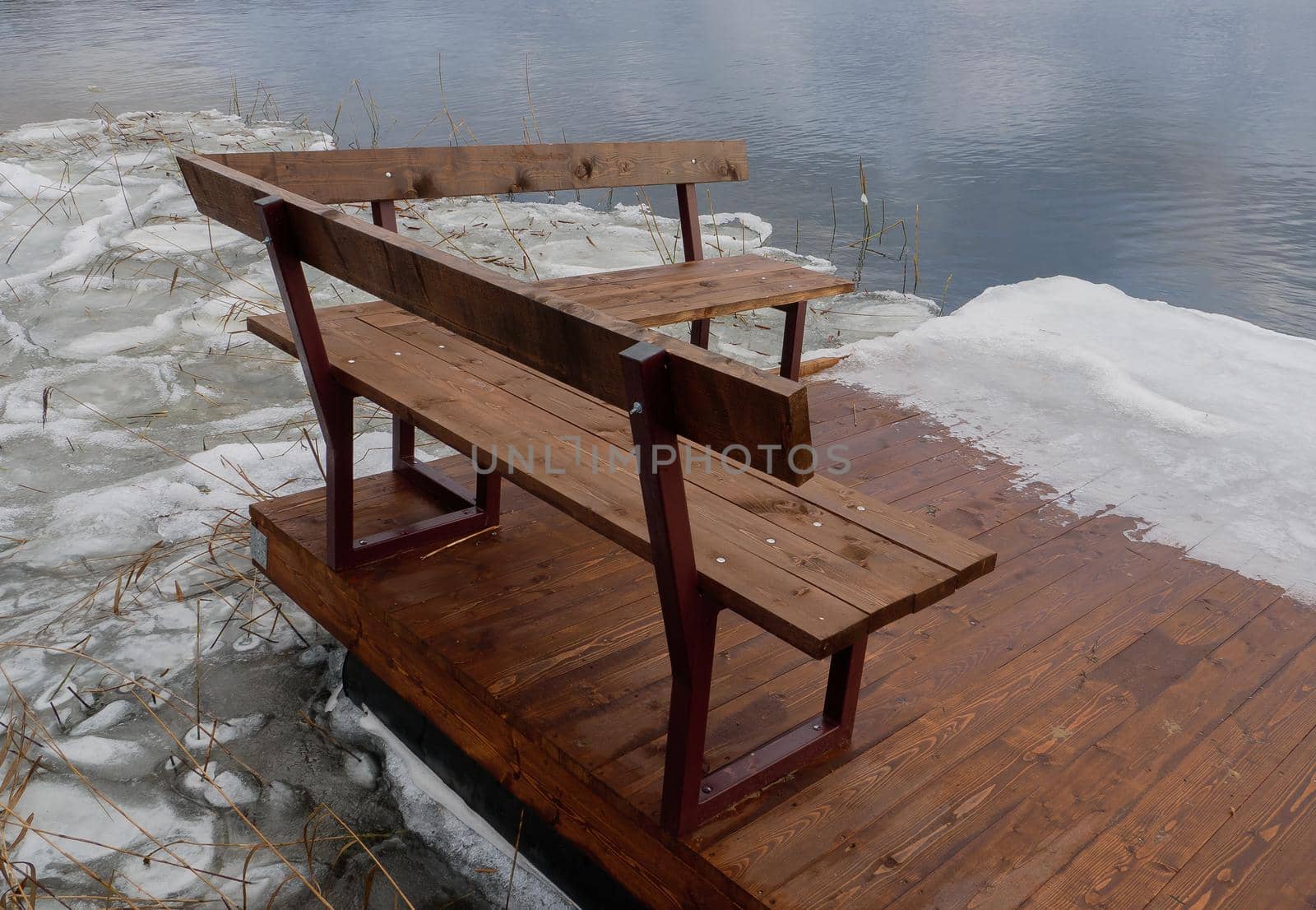 A small wooden pier on the ice of the freezing sea. Bench on the winter shore of the lake. A pier on the winter seashore.