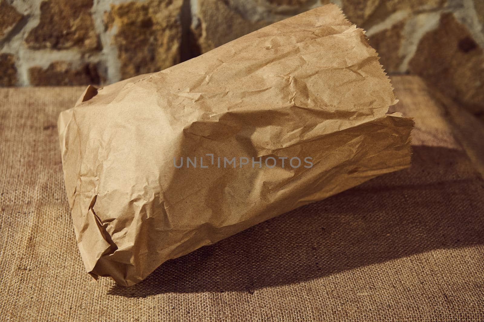 Close-up of an eco-friendly recyclable paper bag with healthy wheat bread inside, on a table with a sackcloth tablecloth by artgf