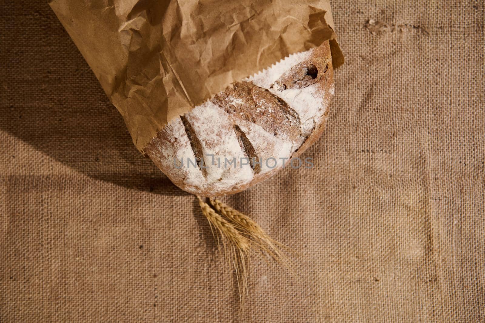 Artisanal bakery. Homemade sourdough bread and ears of wheat on table covered with linen tablecloth. Craft authentic wholesome whole grain rye bread. Home cooking. Food preparation. Selective focus