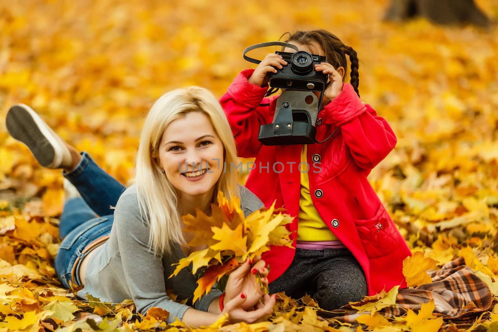 little girl plays with a camera in yellow leaves of autumn landscape