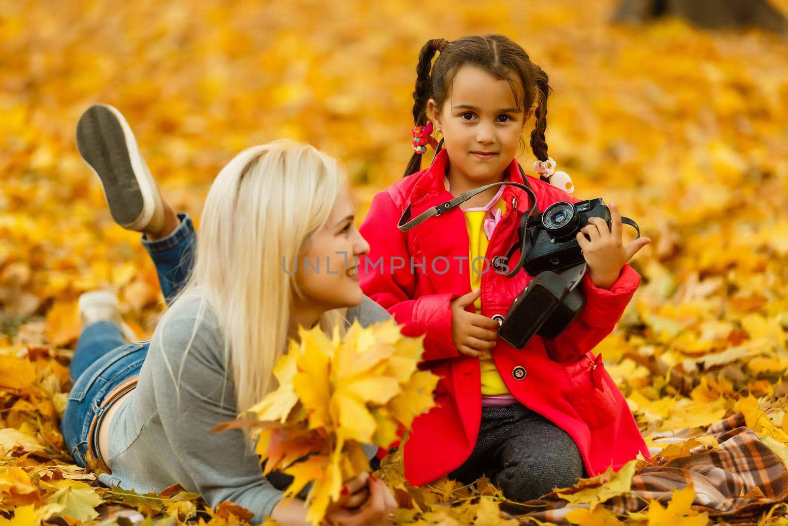 little girl plays with a camera in yellow leaves of autumn landscape