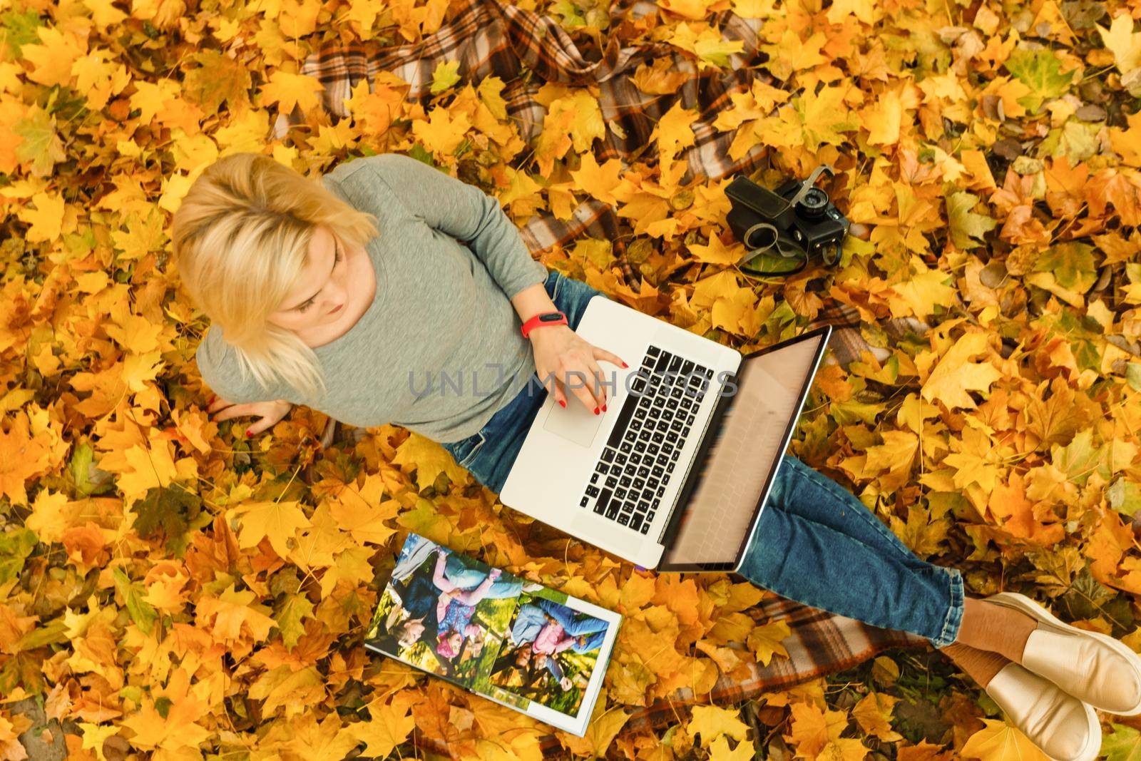 Cute woman with laptop in the autumn park. Beauty nature scene with colorful foliage background, yellow trees and leaves at fall season. Autumn outdoor lifestyle. Happy smiling woman on fall leaves by Andelov13