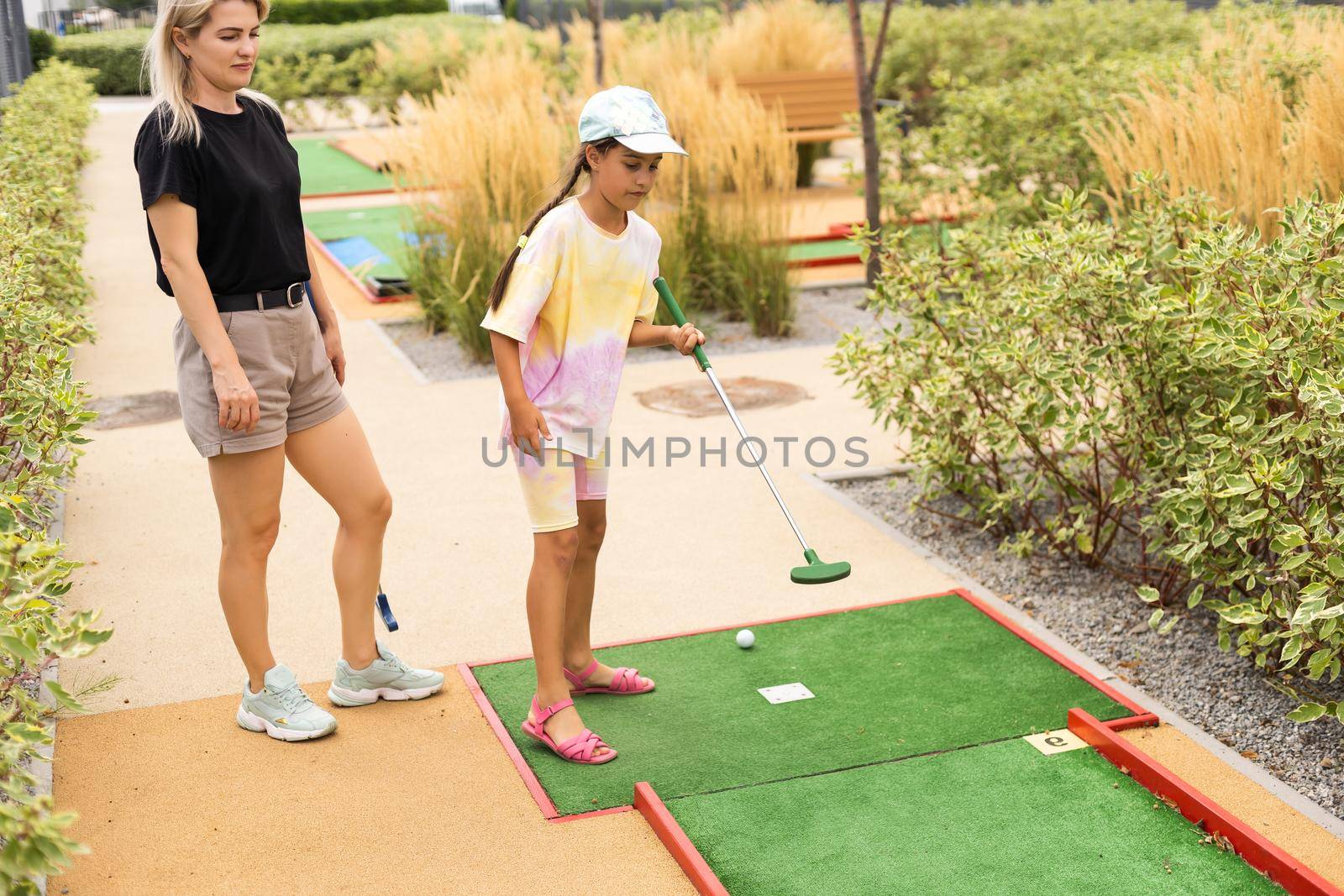 Mother playing with her cute daughter mini golf at outdoor playground