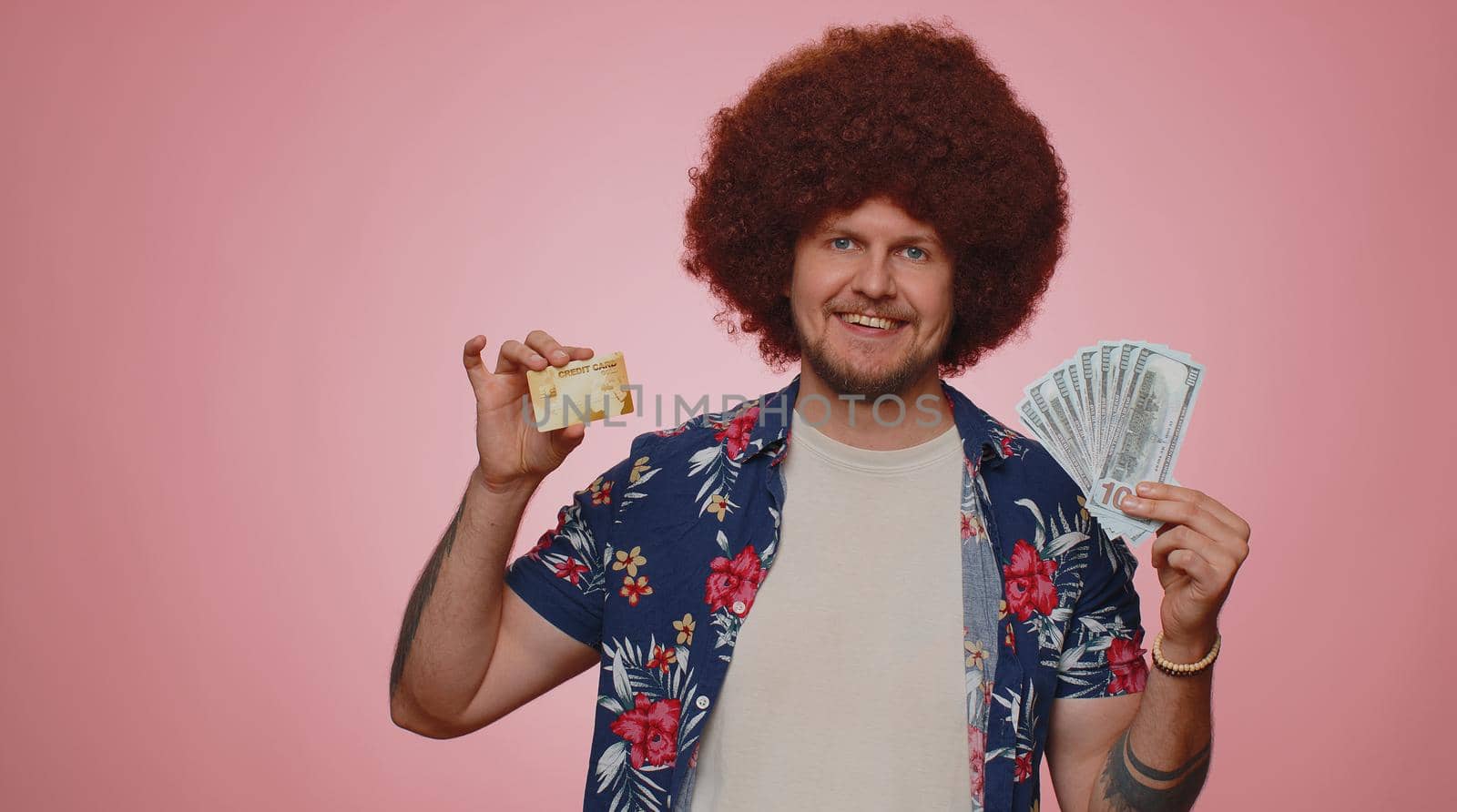Happy tourist man showing plastic credit bank card advertising transferring money cashless, purchases online shopping, sale discount, internet order delivery purchase. Young guy boy on pink background