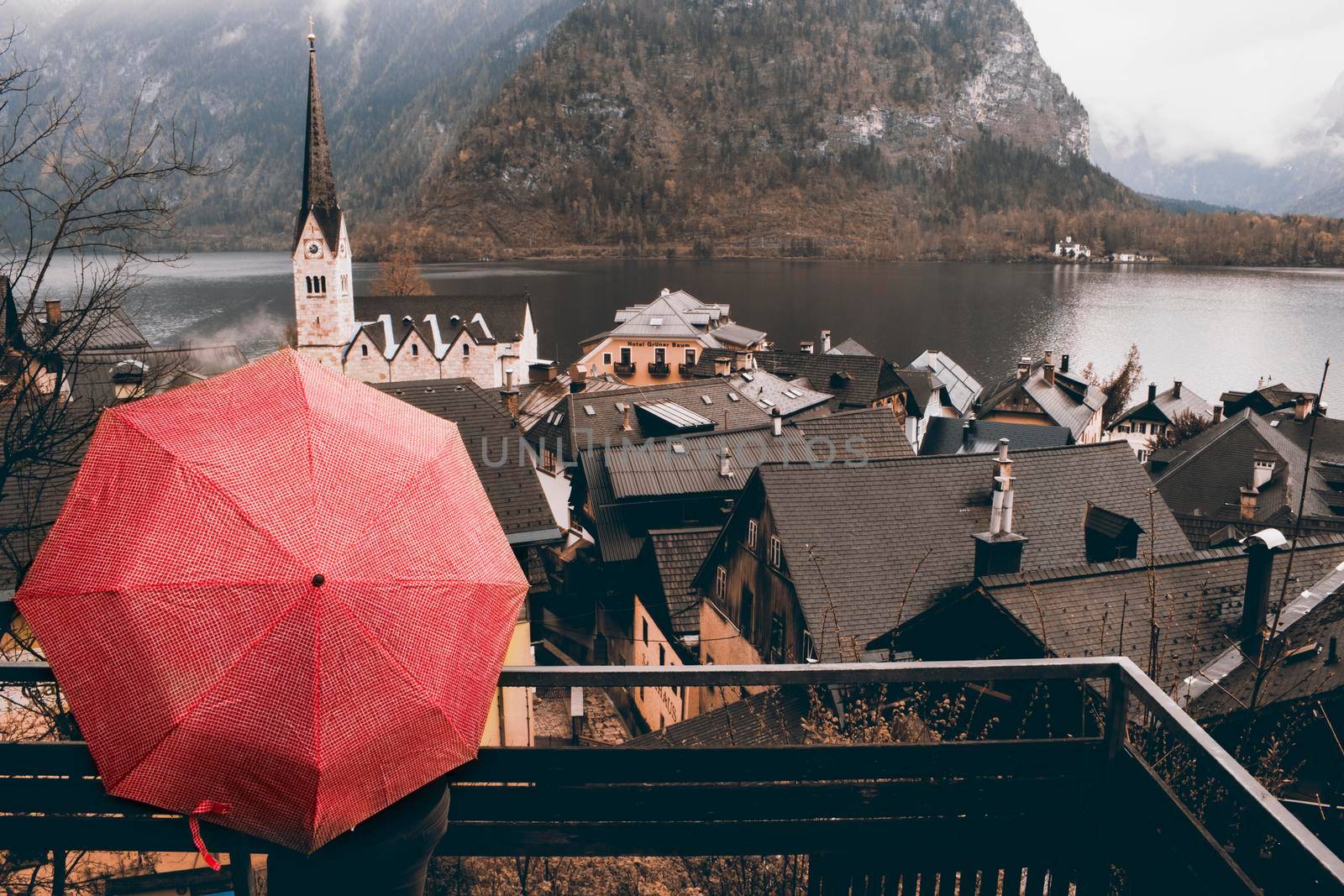 Girl holding a red umbrella looking at Hallstatt tourist town in Austria in a rainy day