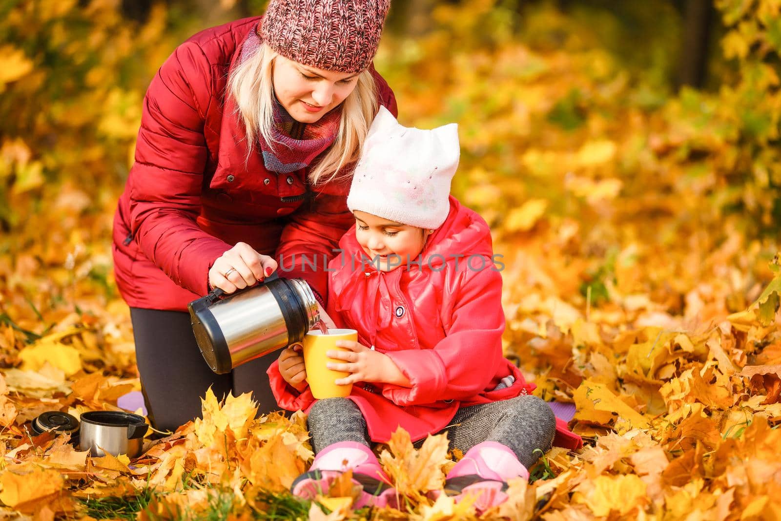 On an autumn walk Mom pours warm tea from her thermos to her daughters. The concept of a family walk.