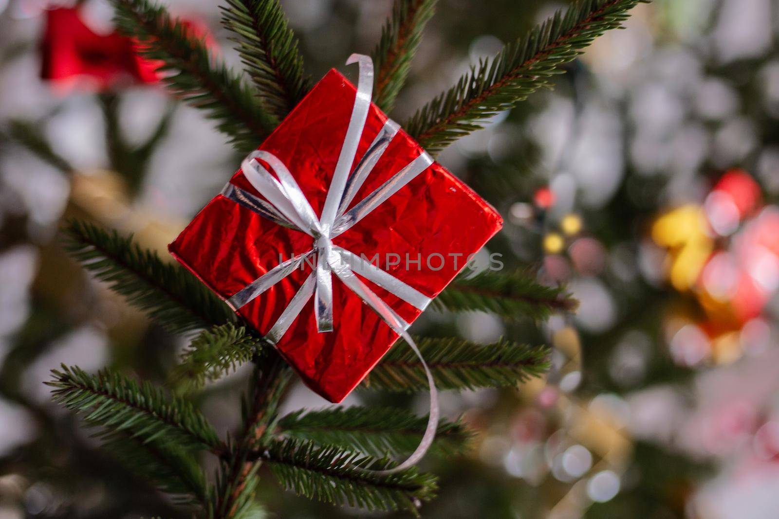 A glittery red gift box on the Christmas tree. Red shiny box hanging on a green Christmas tree.