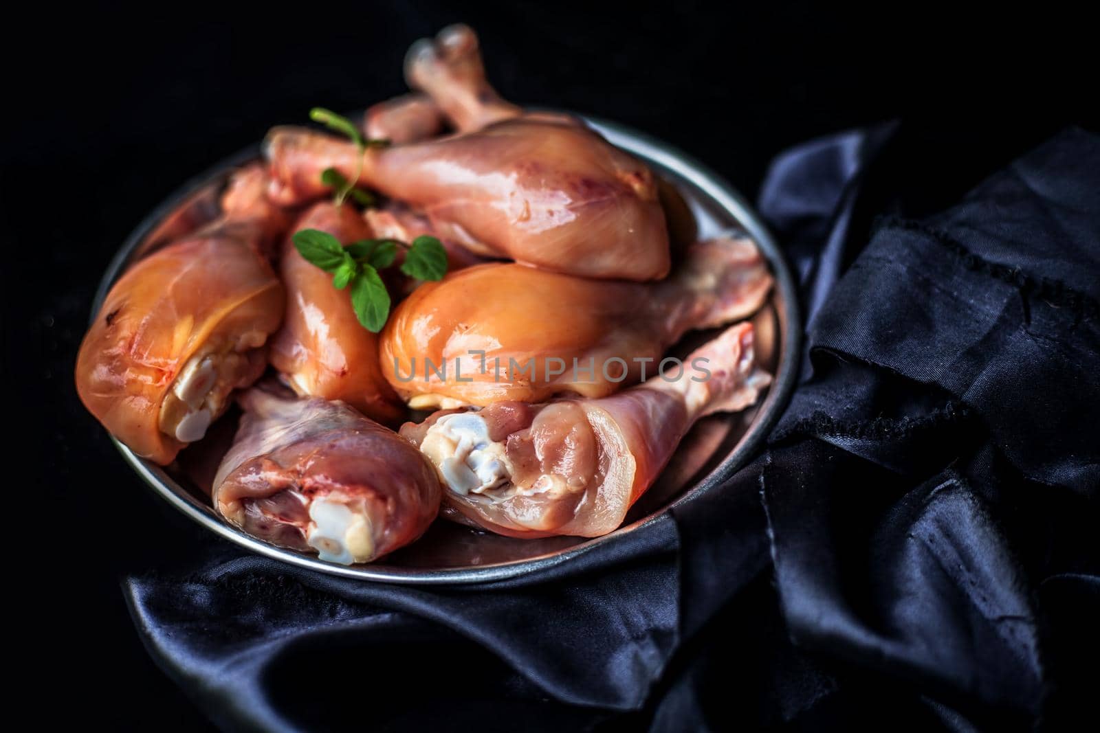 Raw cut chicken drumsticks in a steel plate isolated in black.